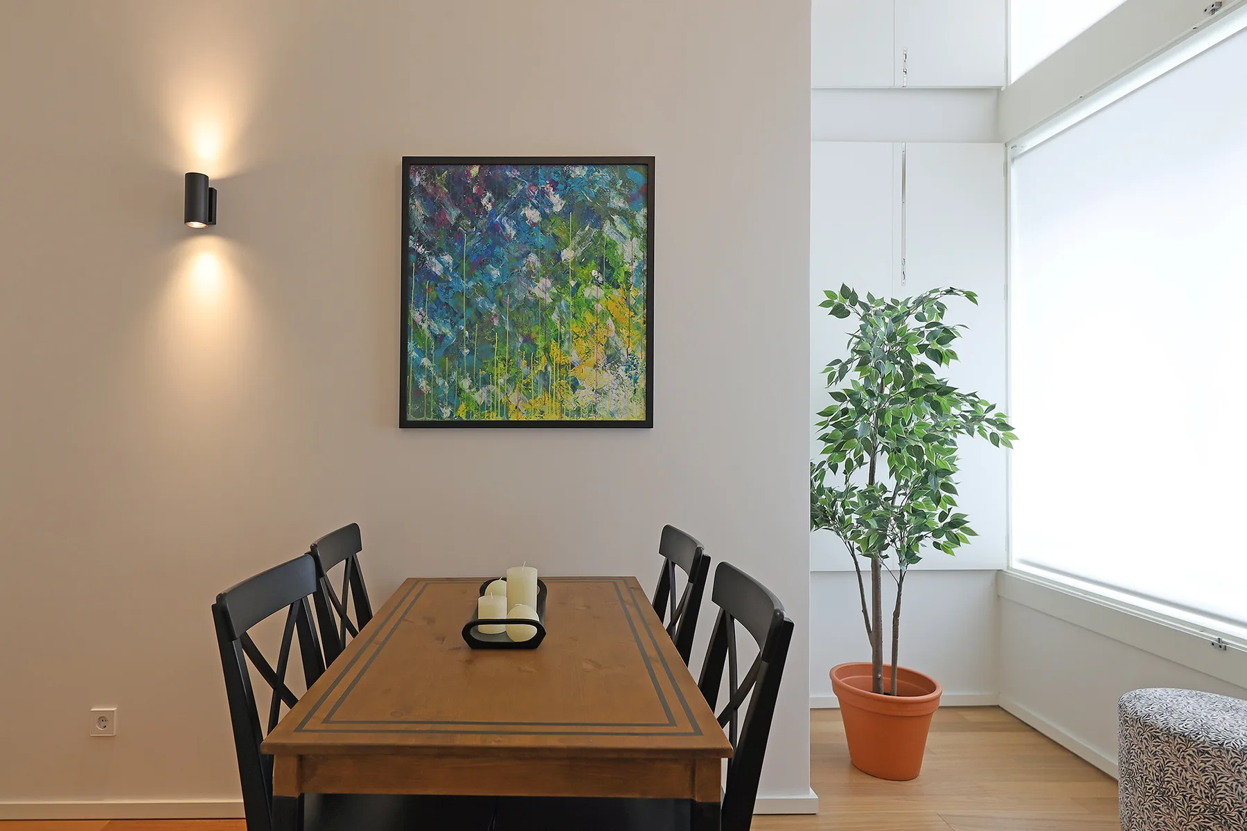A dining area with a wooden table, dark seating, and a potted plant beside a bright window.