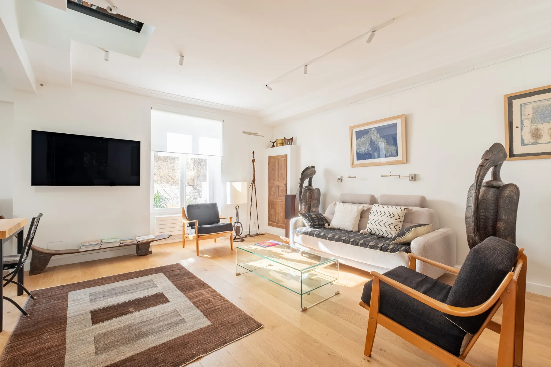 A bright living room with seating, a glass coffee table, and framed artwork.