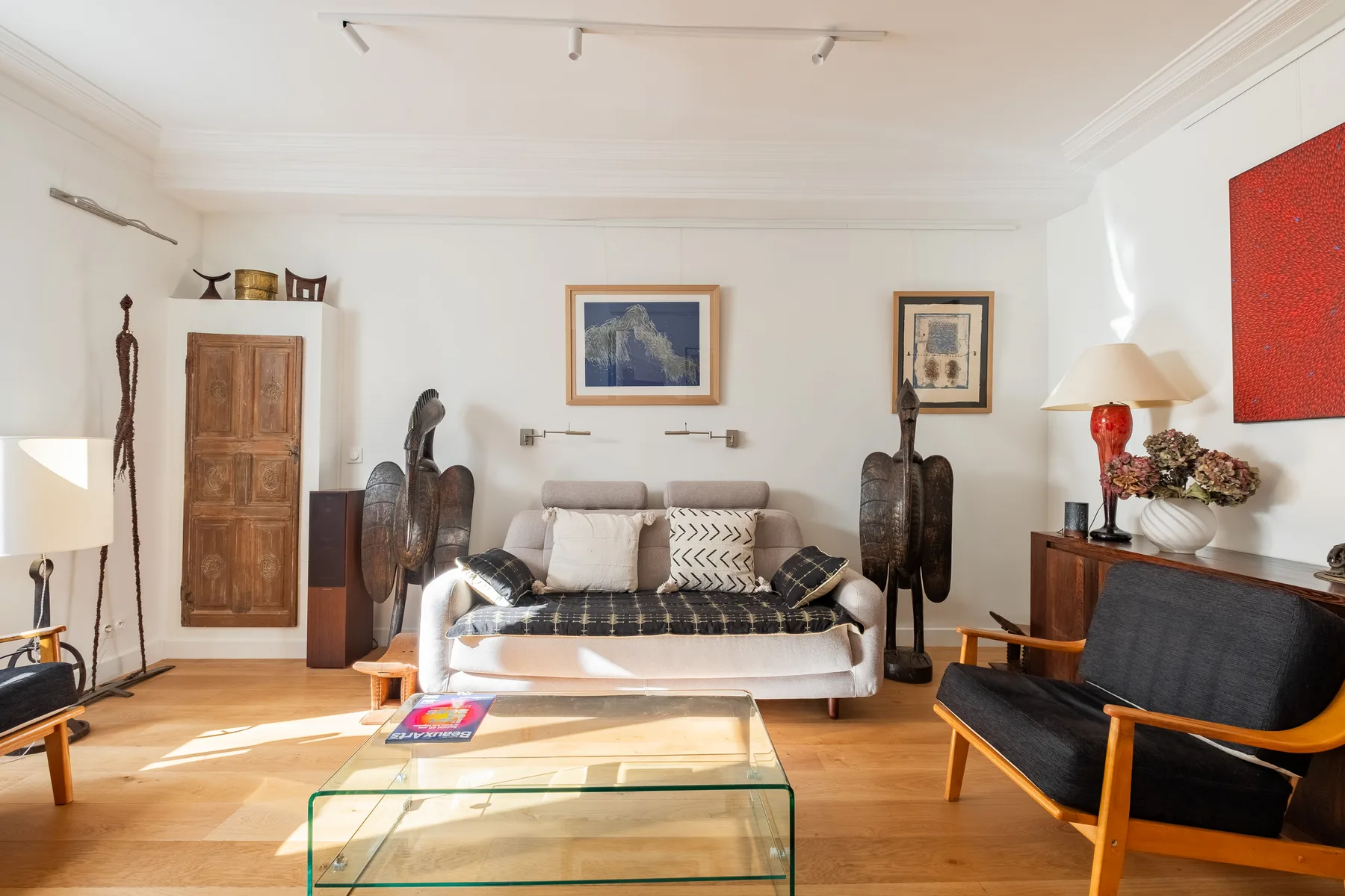 A bright living room features seating around a glass coffee table and framed artwork.