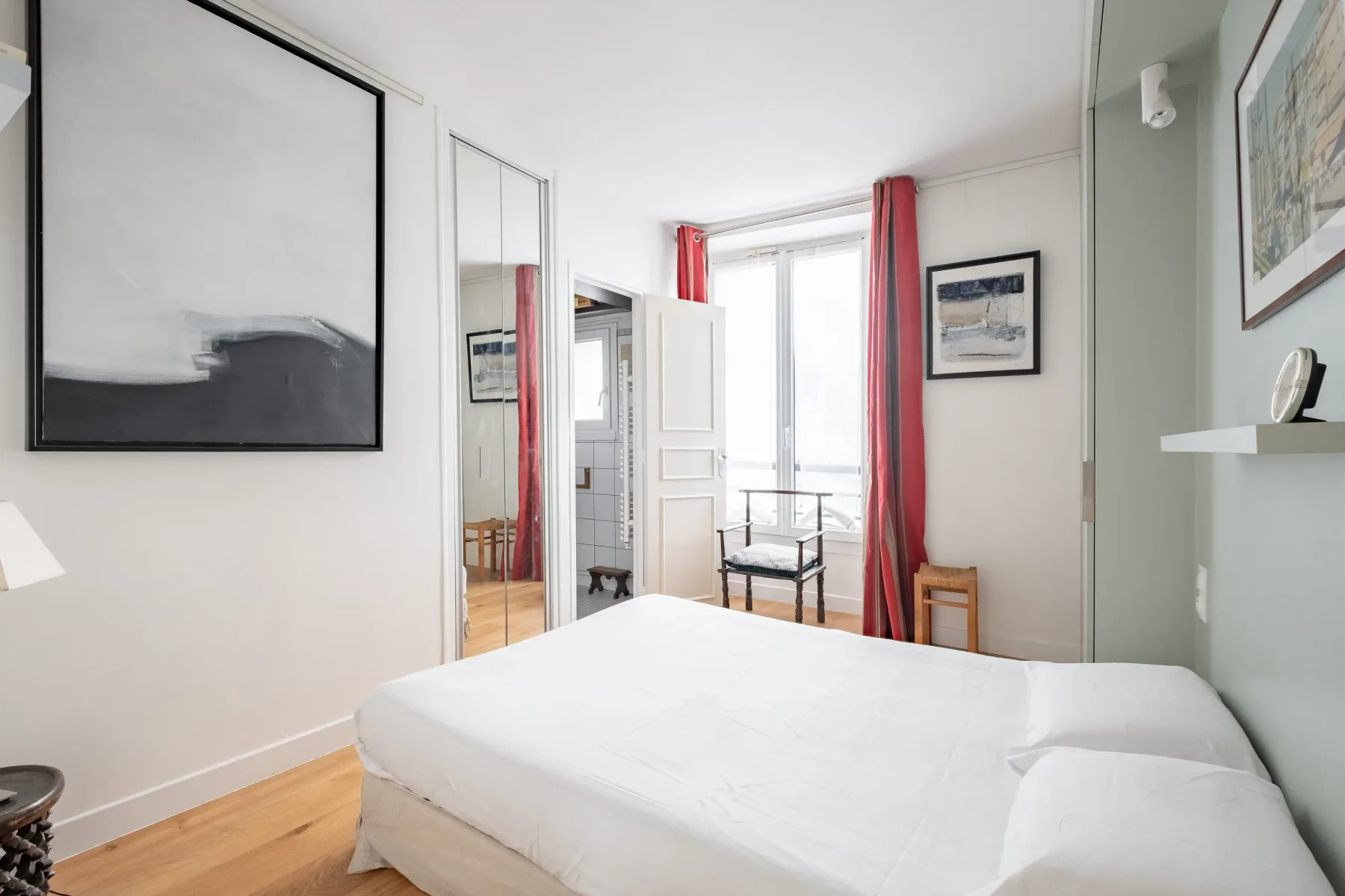A bright bedroom with a white bed and red curtains by the window.