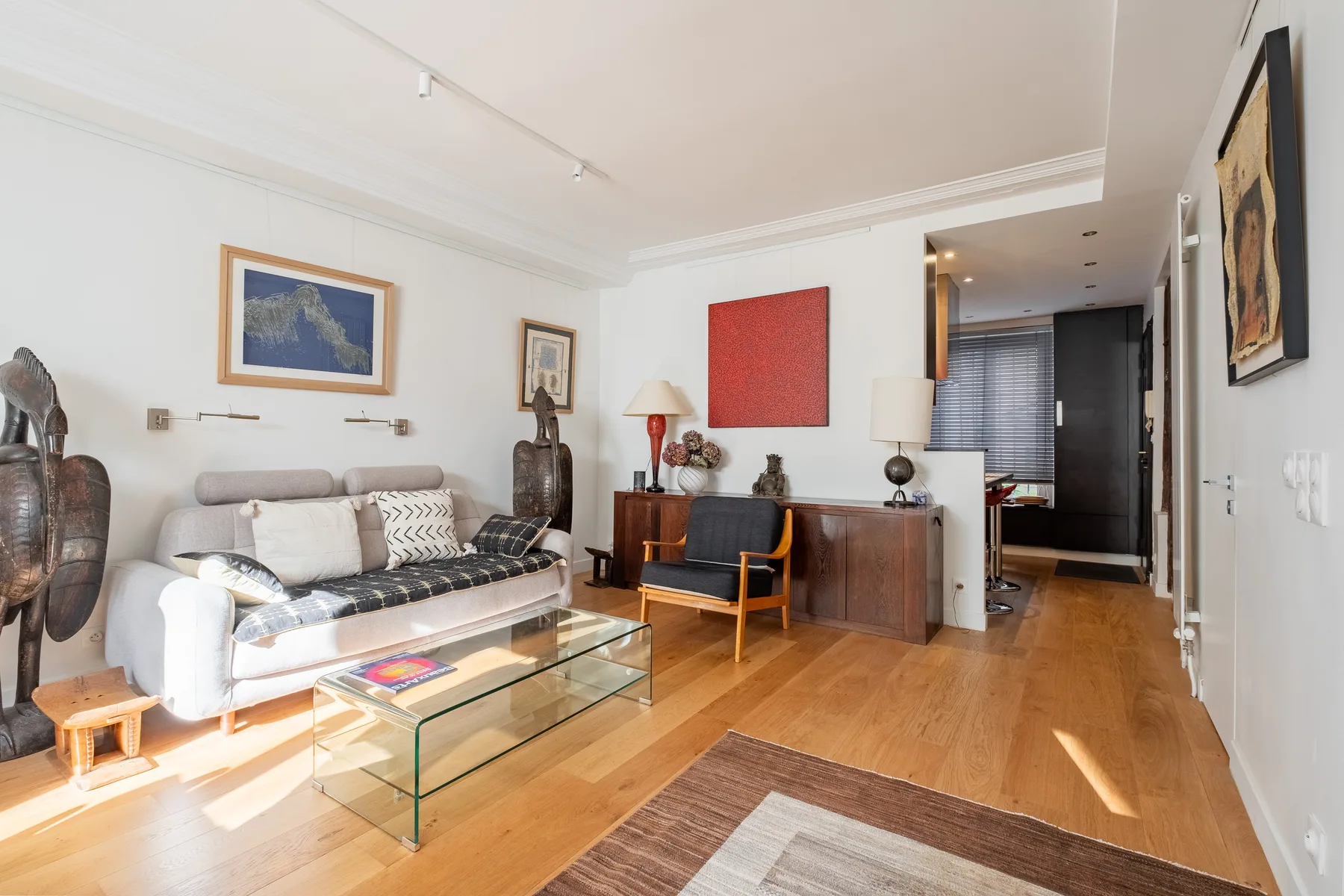 A bright living room with seating, a glass coffee table, and wooden flooring.