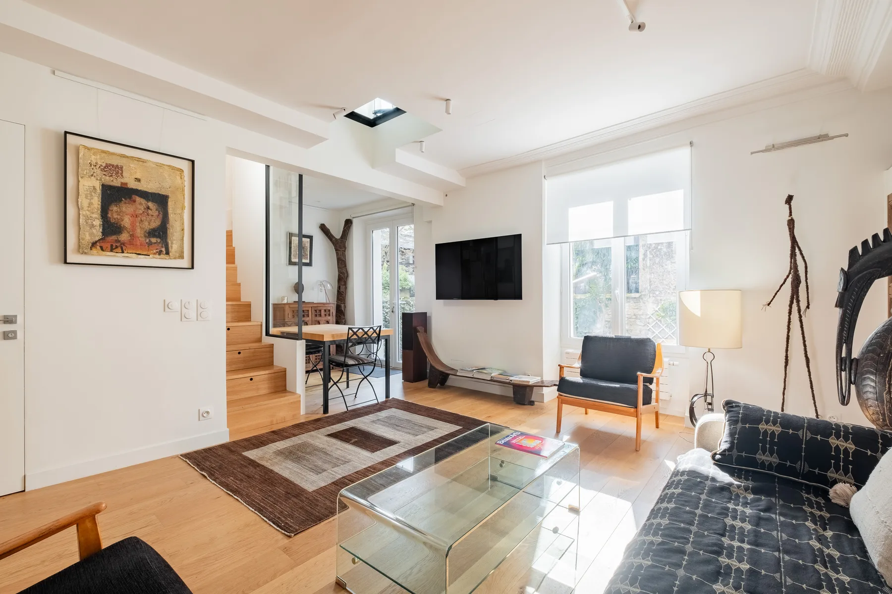 A bright living room with seating, a glass coffee table, and large windows.
