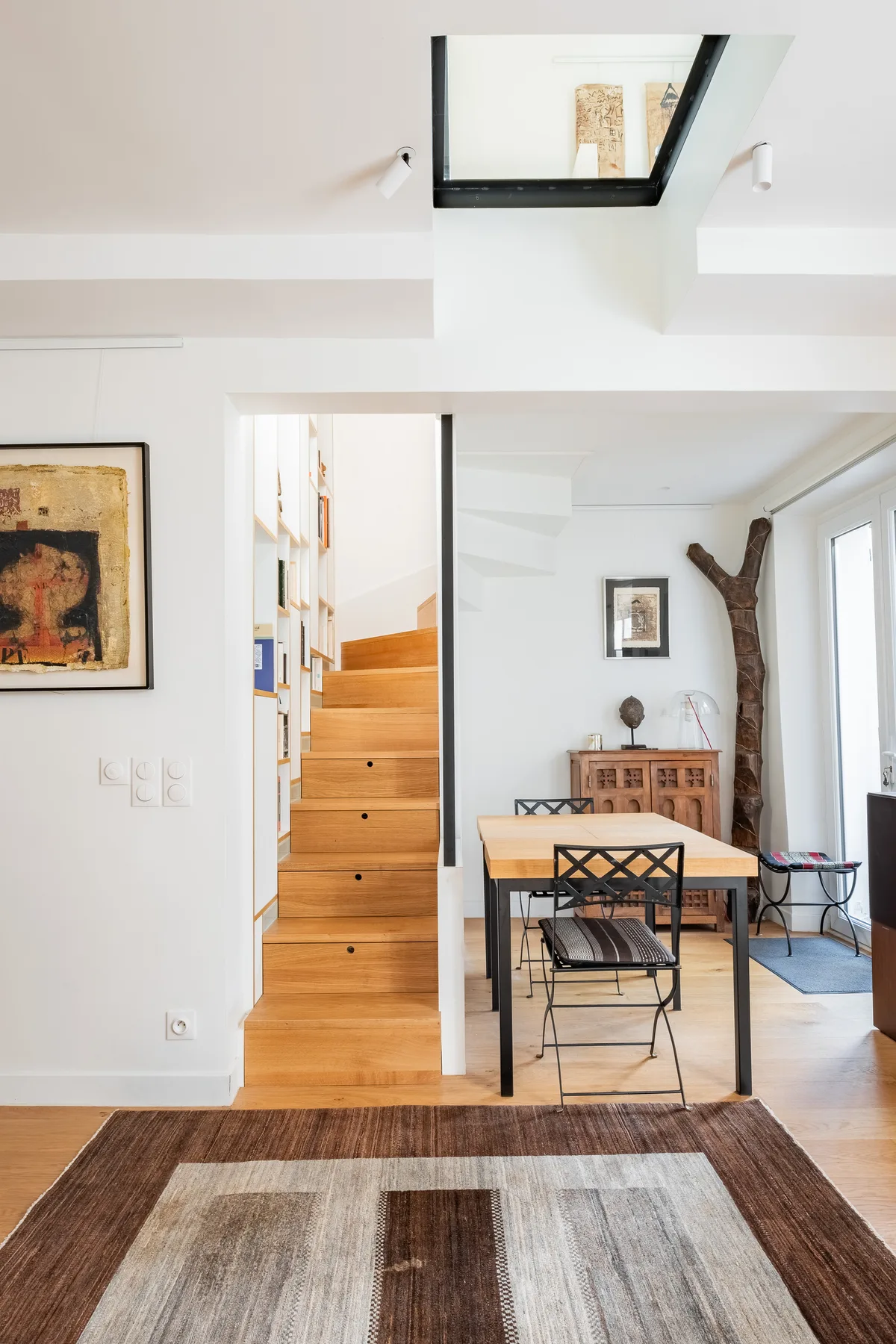 A bright dining area with a wooden table, black chairs, and an open staircase.