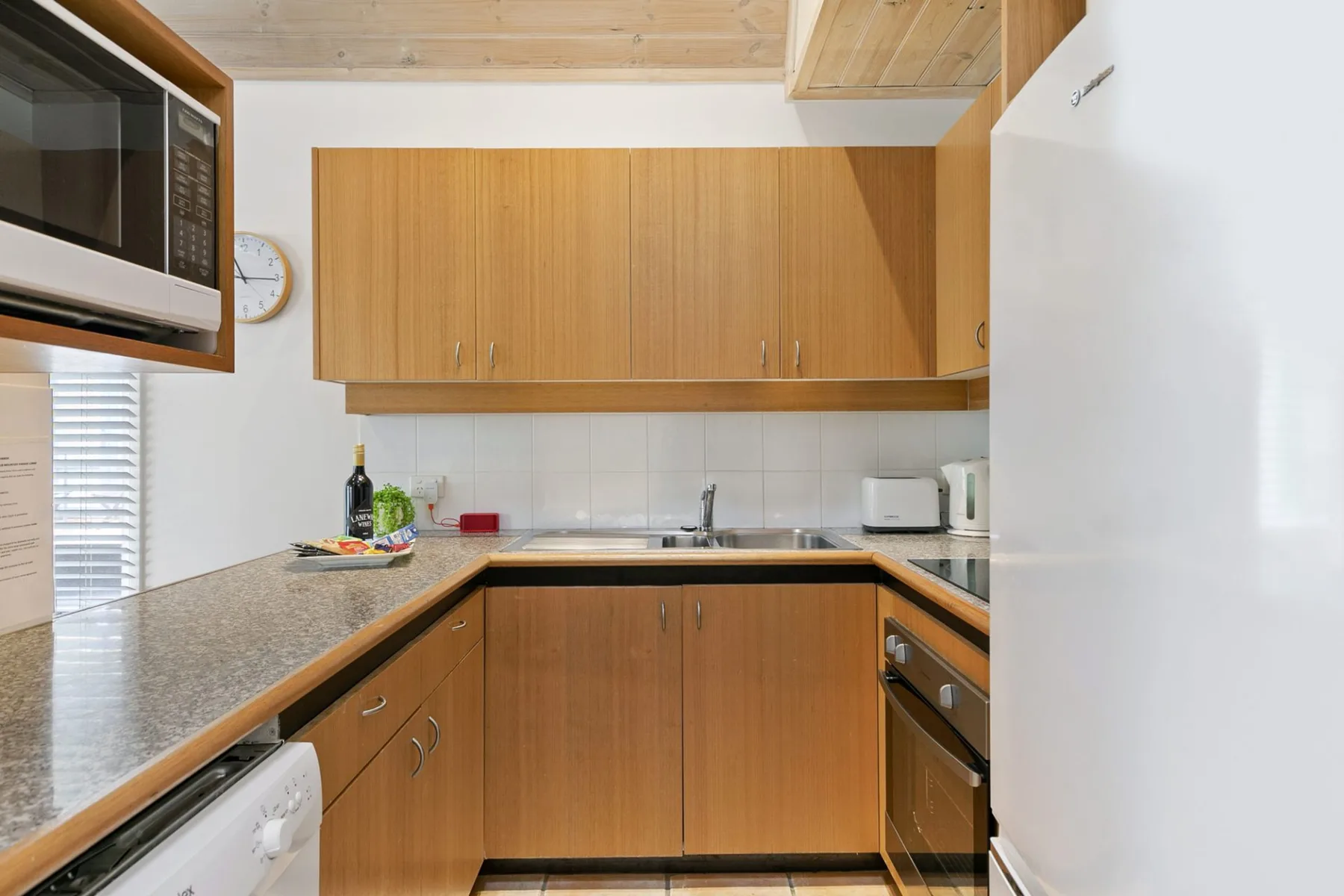 A compact kitchen with wooden cabinets, counters, and built-in appliances.