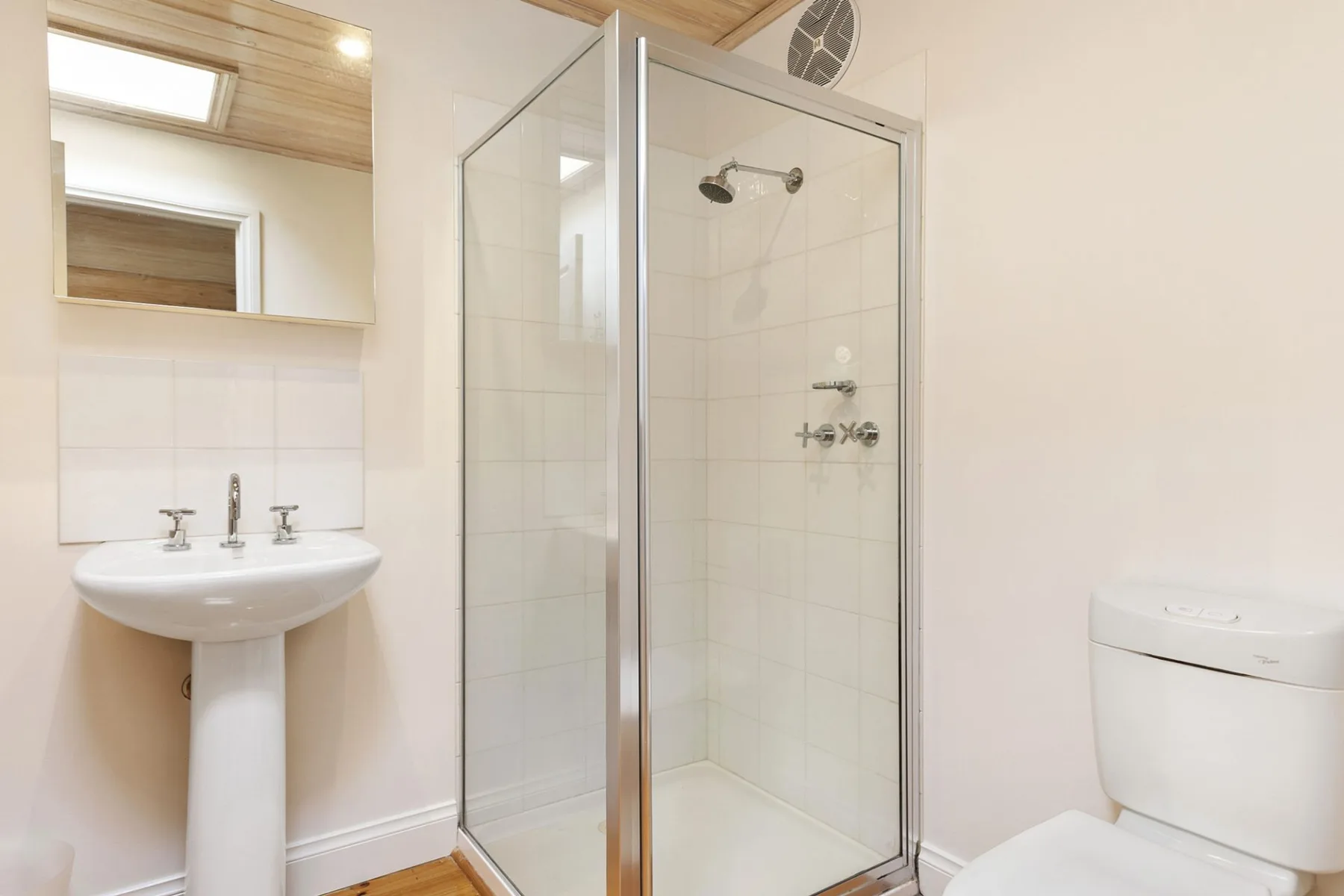 A bright bathroom with a glass shower and pedestal sink.