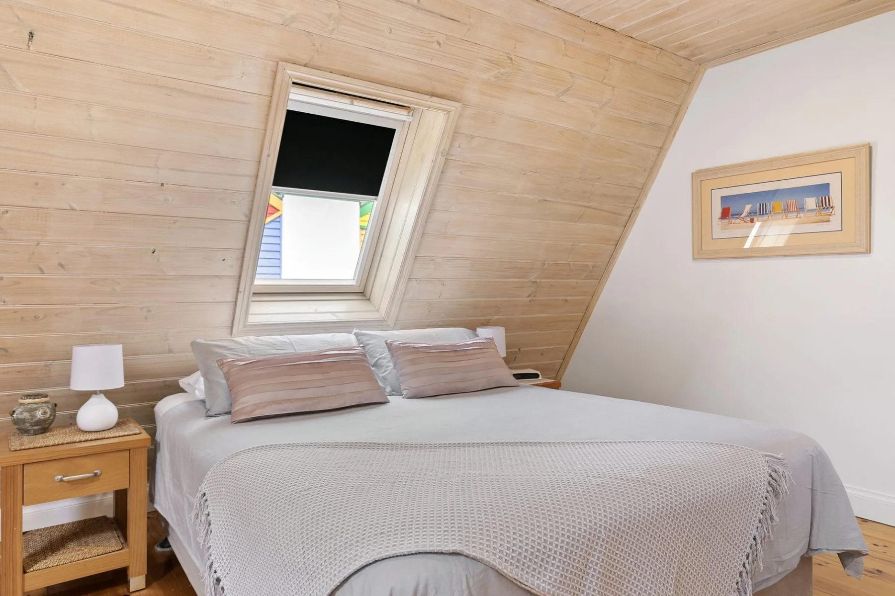 A bedroom with a bed beneath a sloped wooden ceiling and skylight.