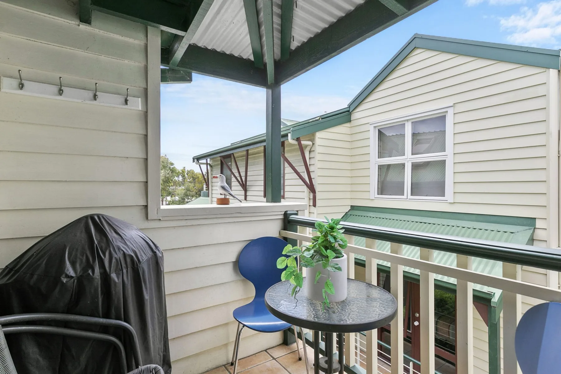 A covered balcony with a small table and seating overlooks a neighboring building.