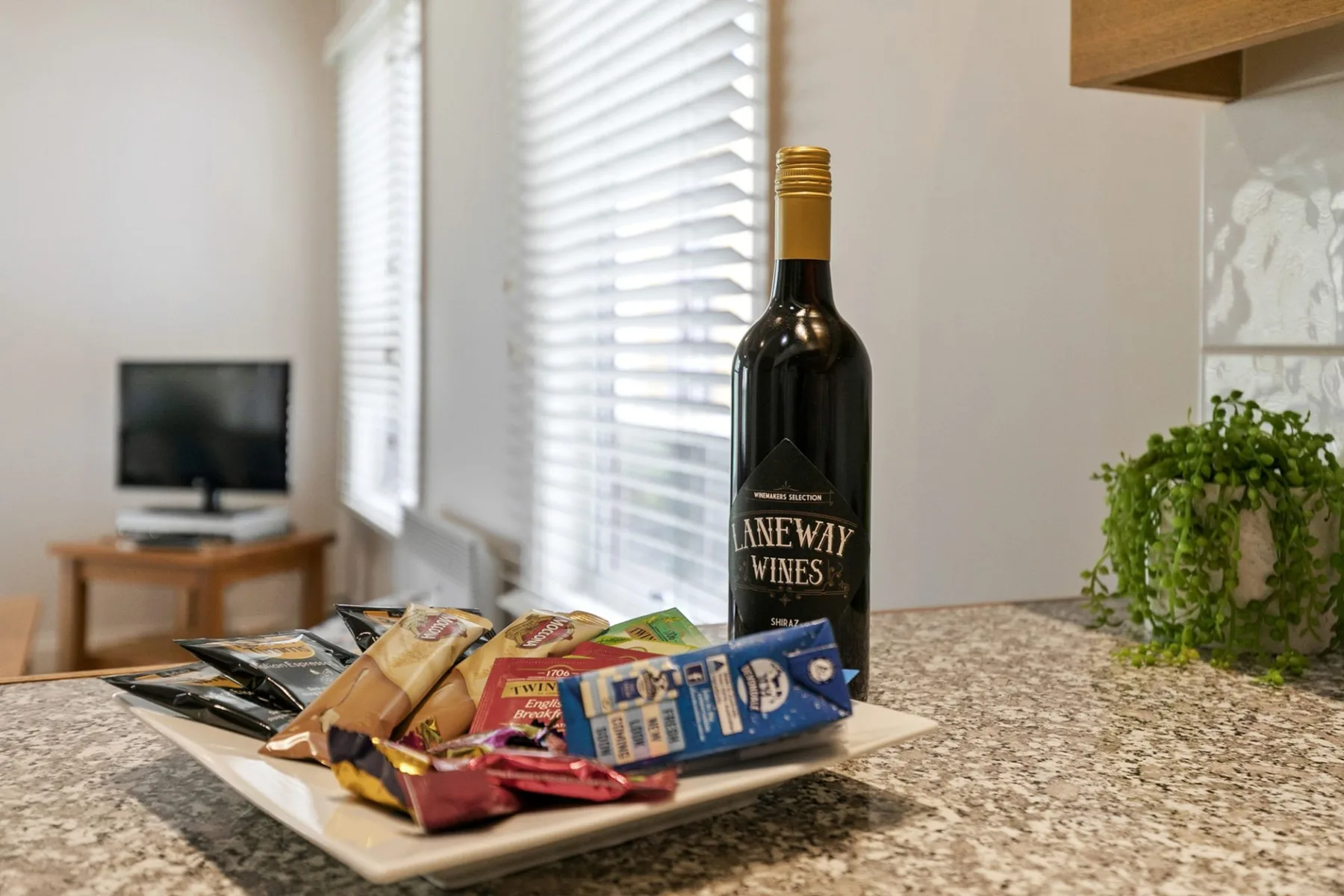 A kitchen counter displays a bottle of wine and a plate of packaged snacks.