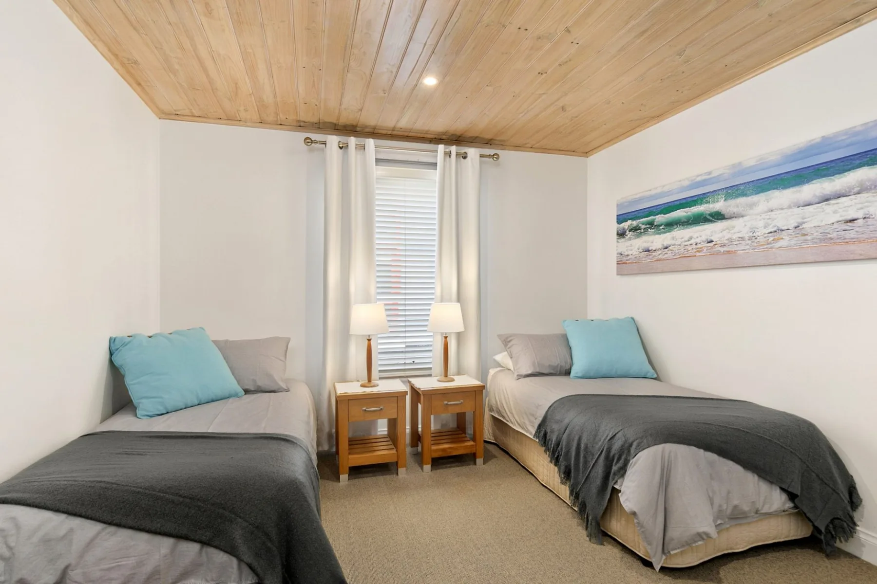 A bedroom with two beds, bedside tables, and a window with white curtains.