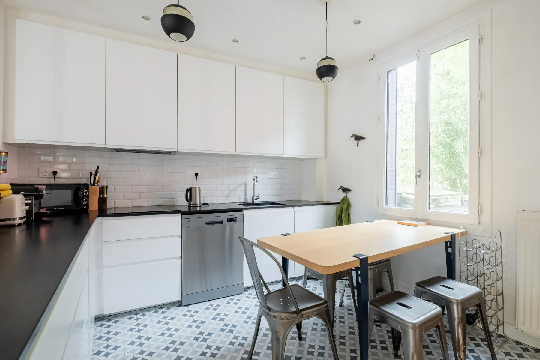 A bright kitchen with white cabinets, dark counters, and a dining table.