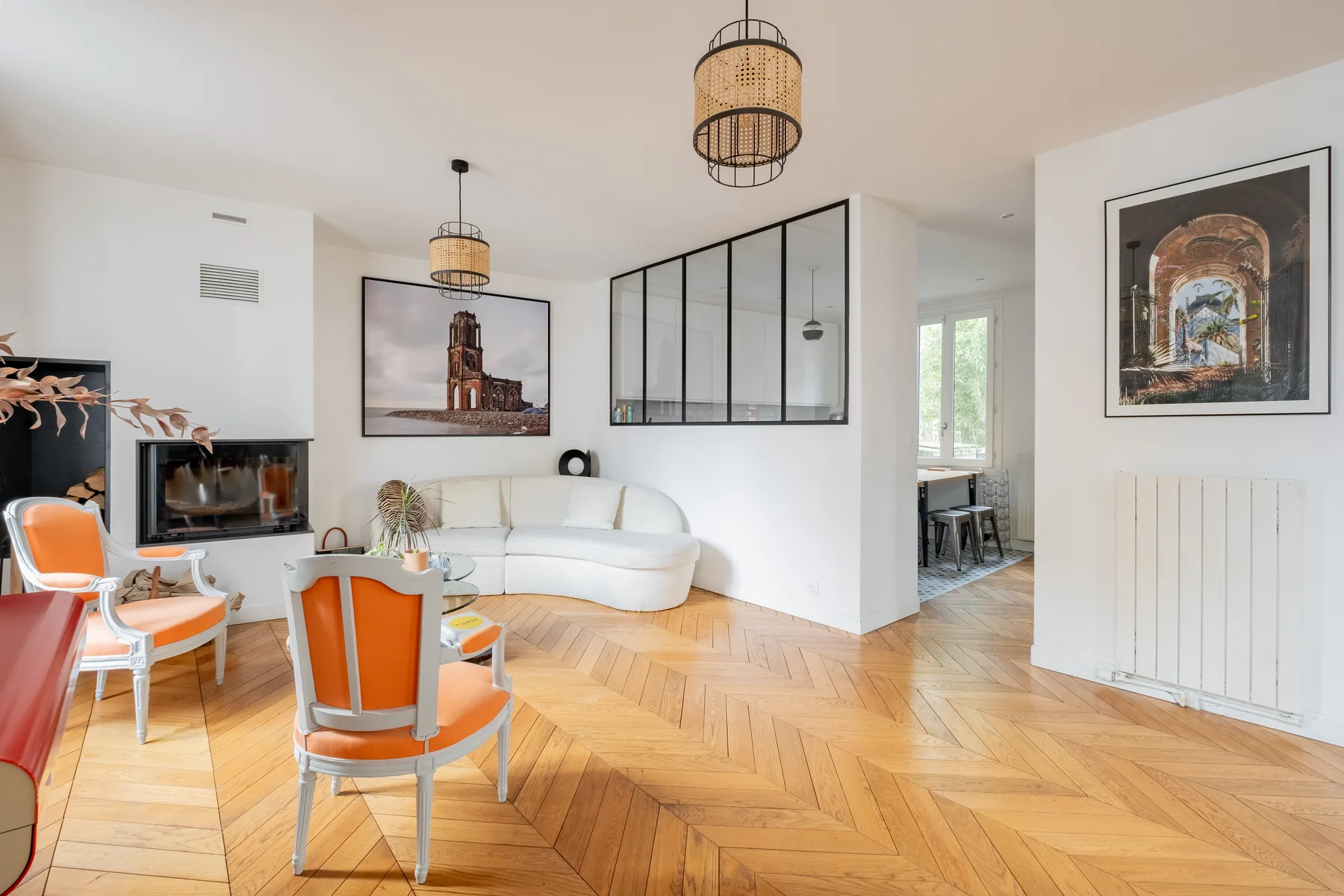 A bright living room with seating, framed artwork, and a herringbone wood floor.