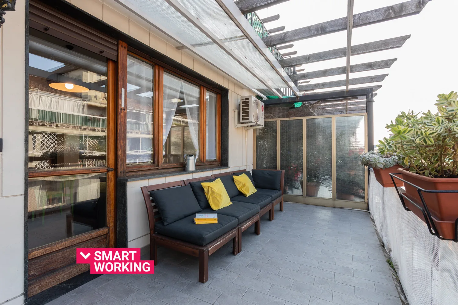 A covered patio with outdoor seating and potted plants beside glass doors.