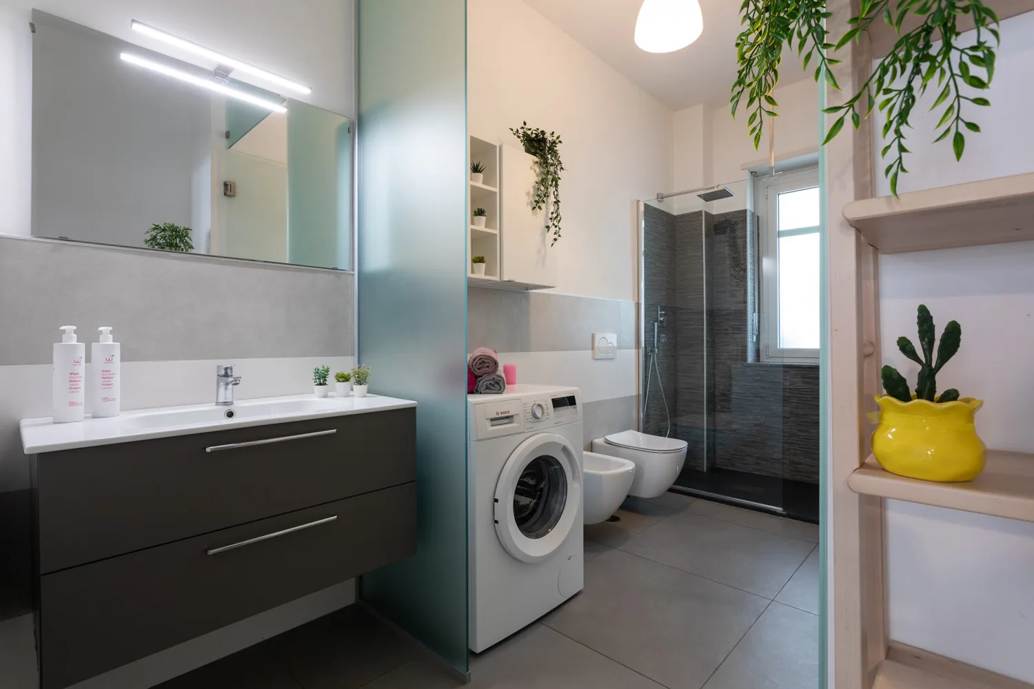 A modern bathroom with a vanity, washing machine, and glass shower.