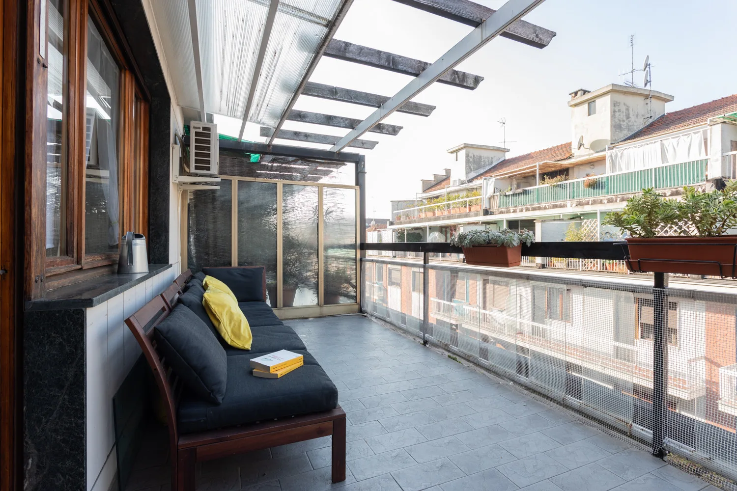 A rooftop terrace with cushioned seating and a glass canopy.