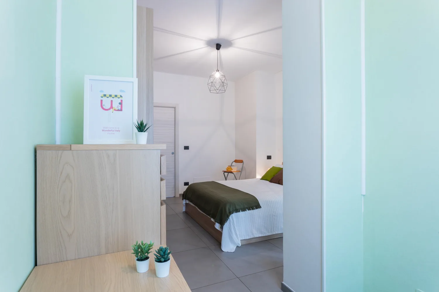 A bedroom with a bed, light wood furniture, and a hanging pendant light.