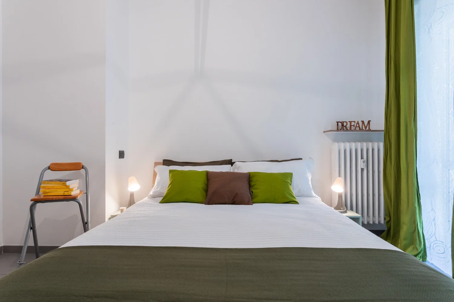 Bedroom with a neatly made bed and green curtains beside the window.