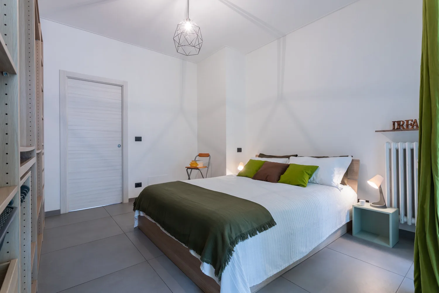 A bedroom with a bed dressed in white linens and green cushions.