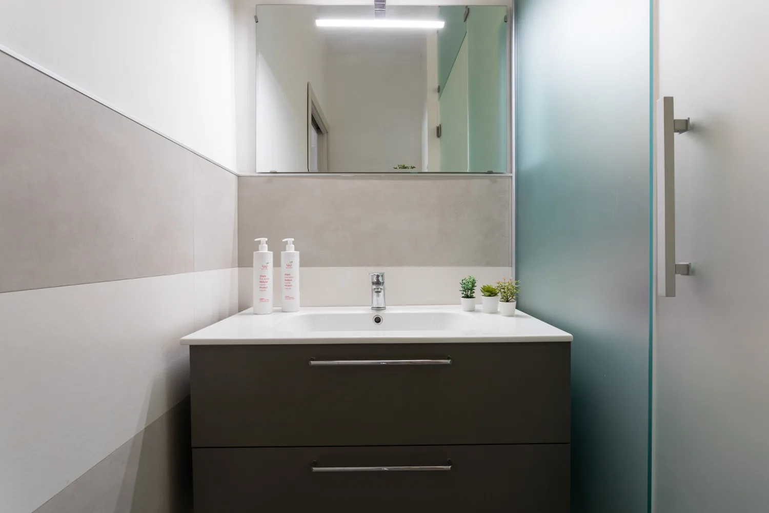 A modern bathroom vanity with a wide mirror and frosted glass shower screen.