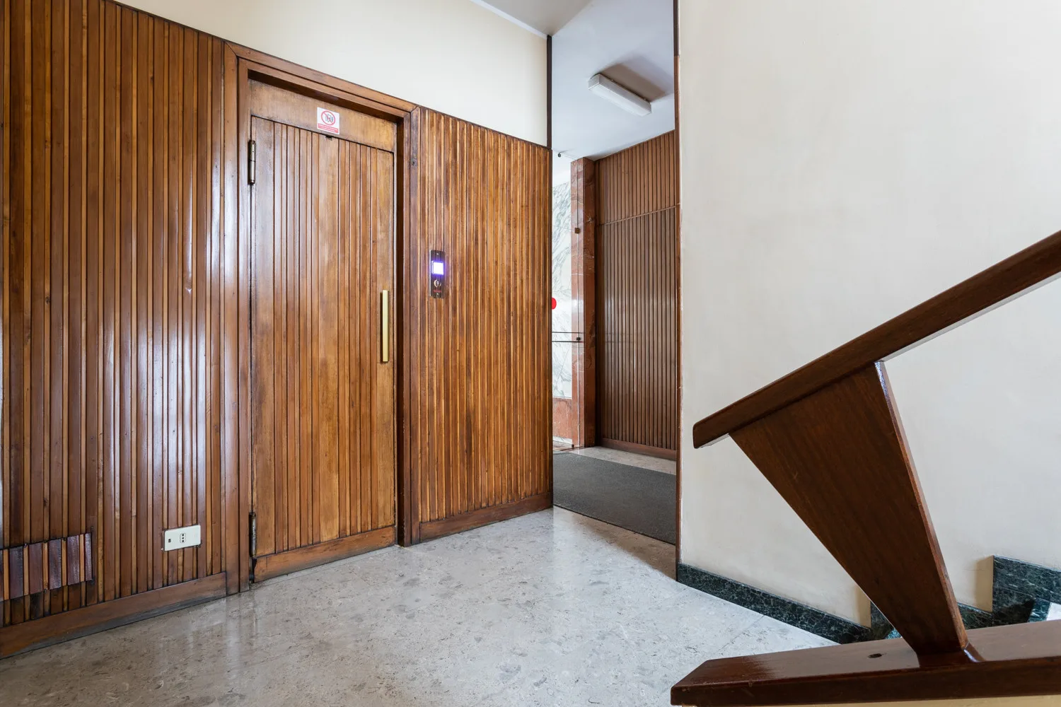 A wood-paneled hallway with a door and a staircase railing.