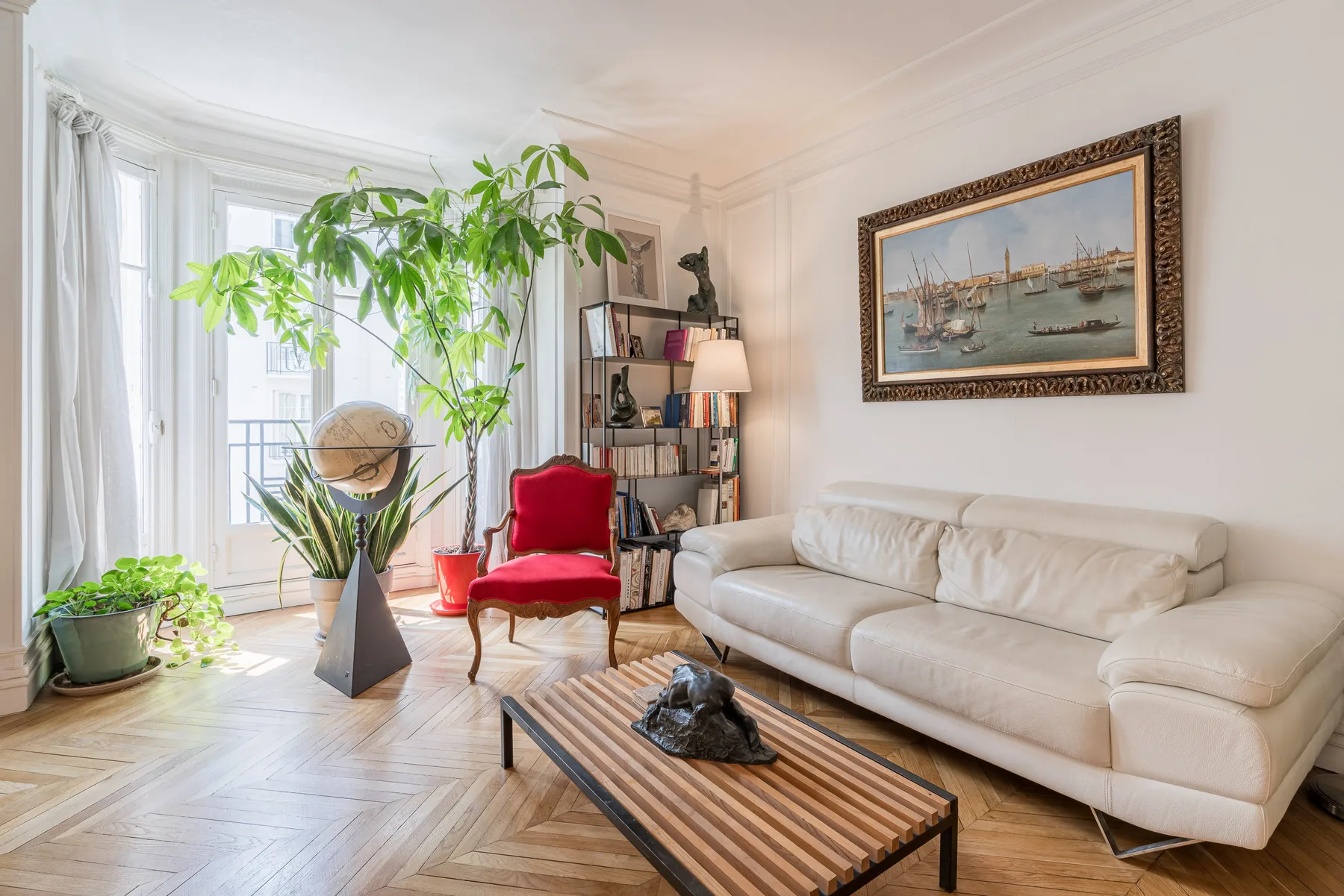 Una luminosa sala de estar con sofá blanco, sillón rojo y plantas frondosas.