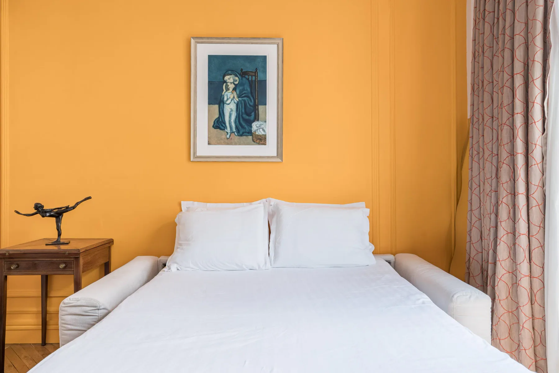 Un dormitorio con una cama tendida bajo un cuadro enmarcado.