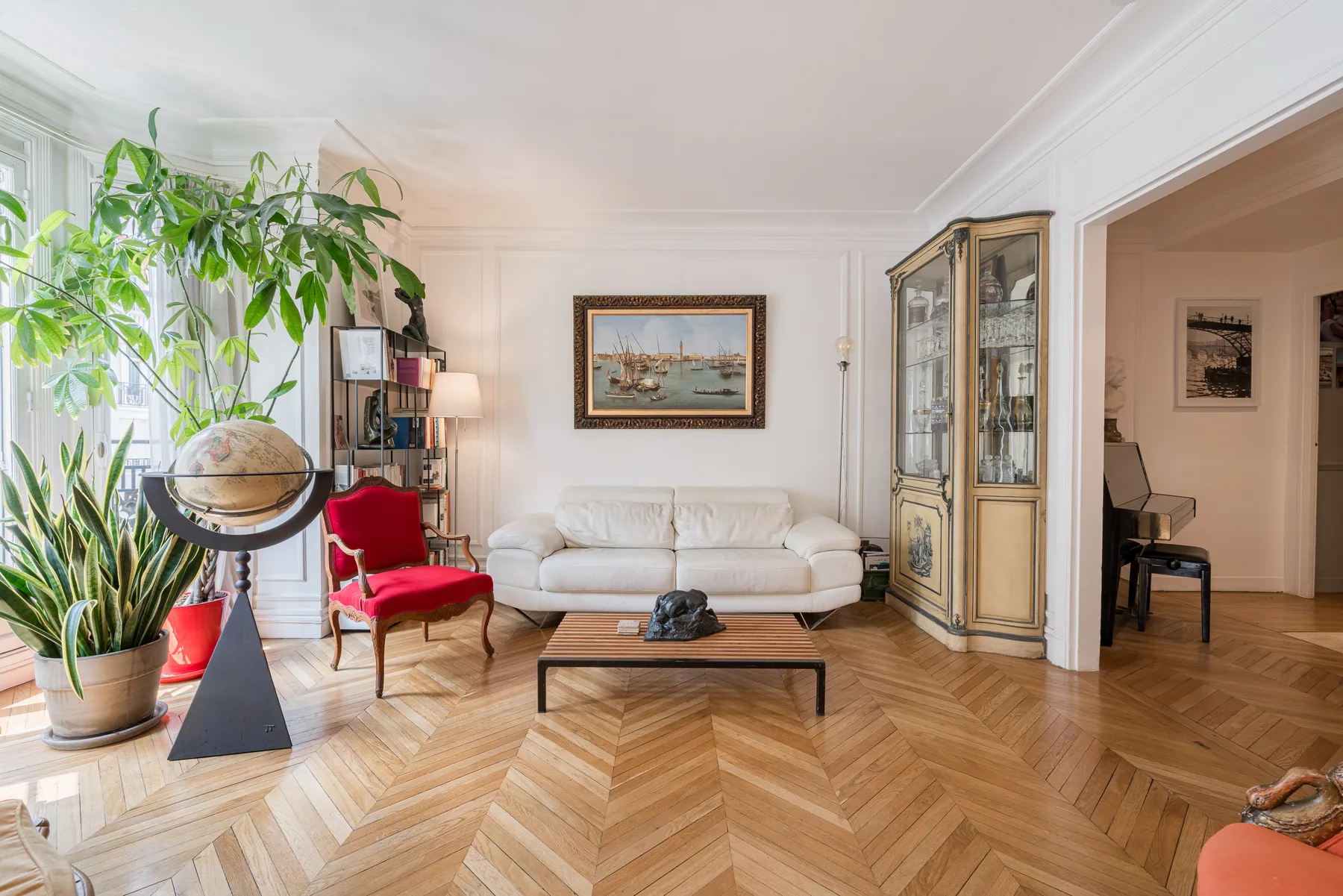 Una sala luminosa con asientos blancos, plantas frondosas y un cuadro enmarcado.