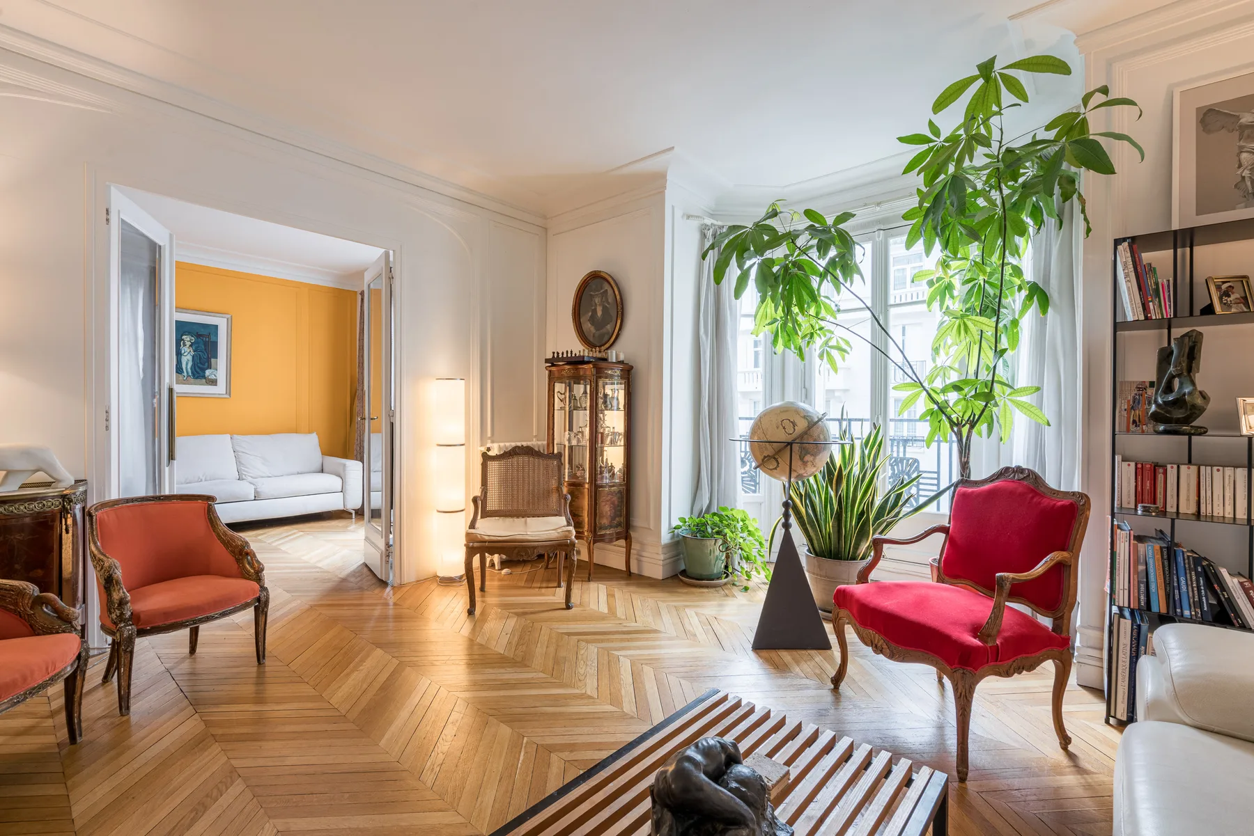 Una sala luminosa con asientos rojos, plantas altas y una ventana grande.