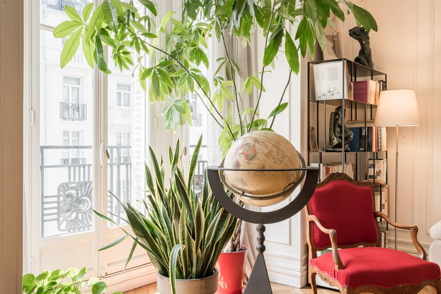 Una sala de estar luminosa con un sillón rojo, un globo terráqueo y plantas junto a las ventanas.