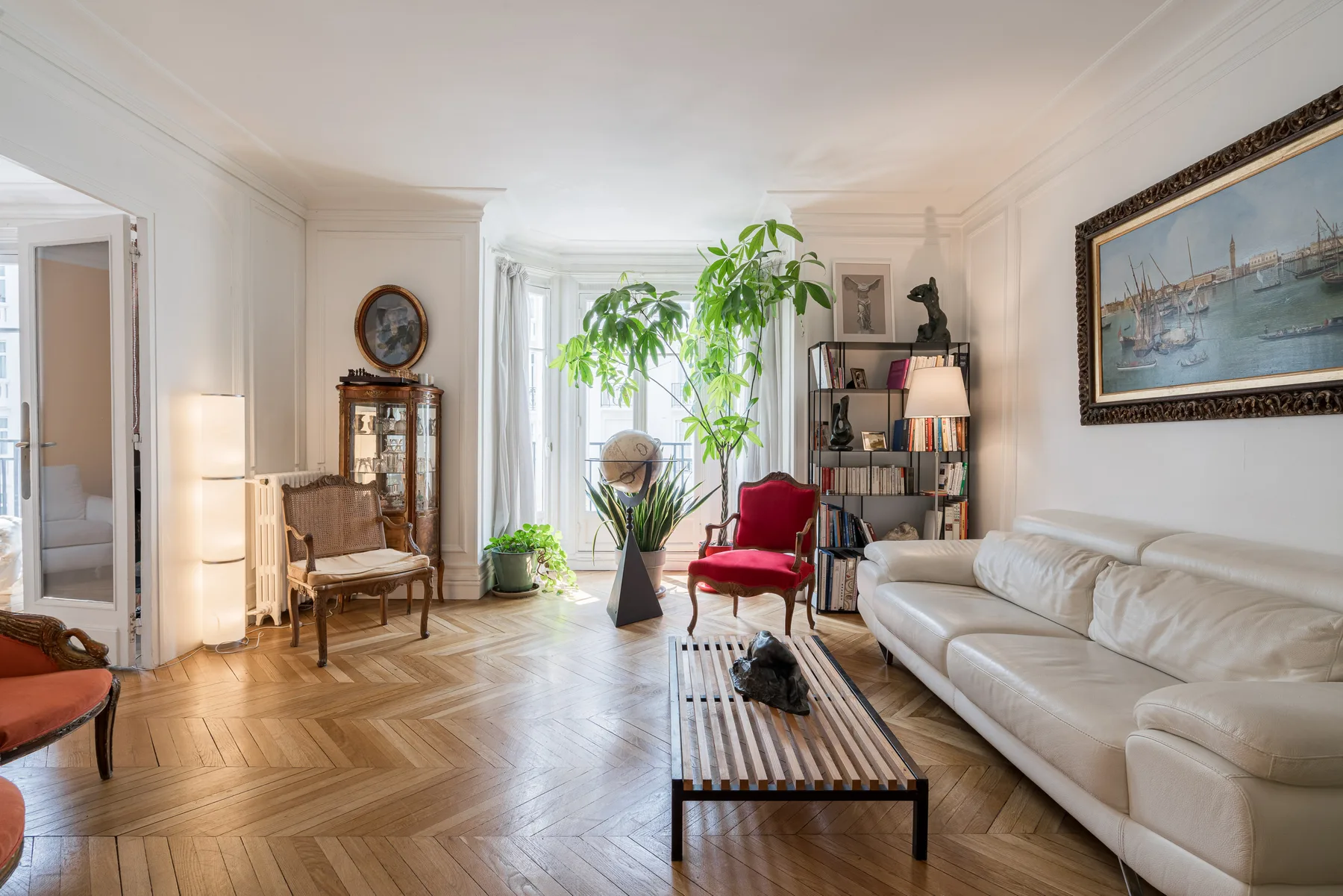 Una sala luminosa con un sofá blanco y una planta grande en una maceta.