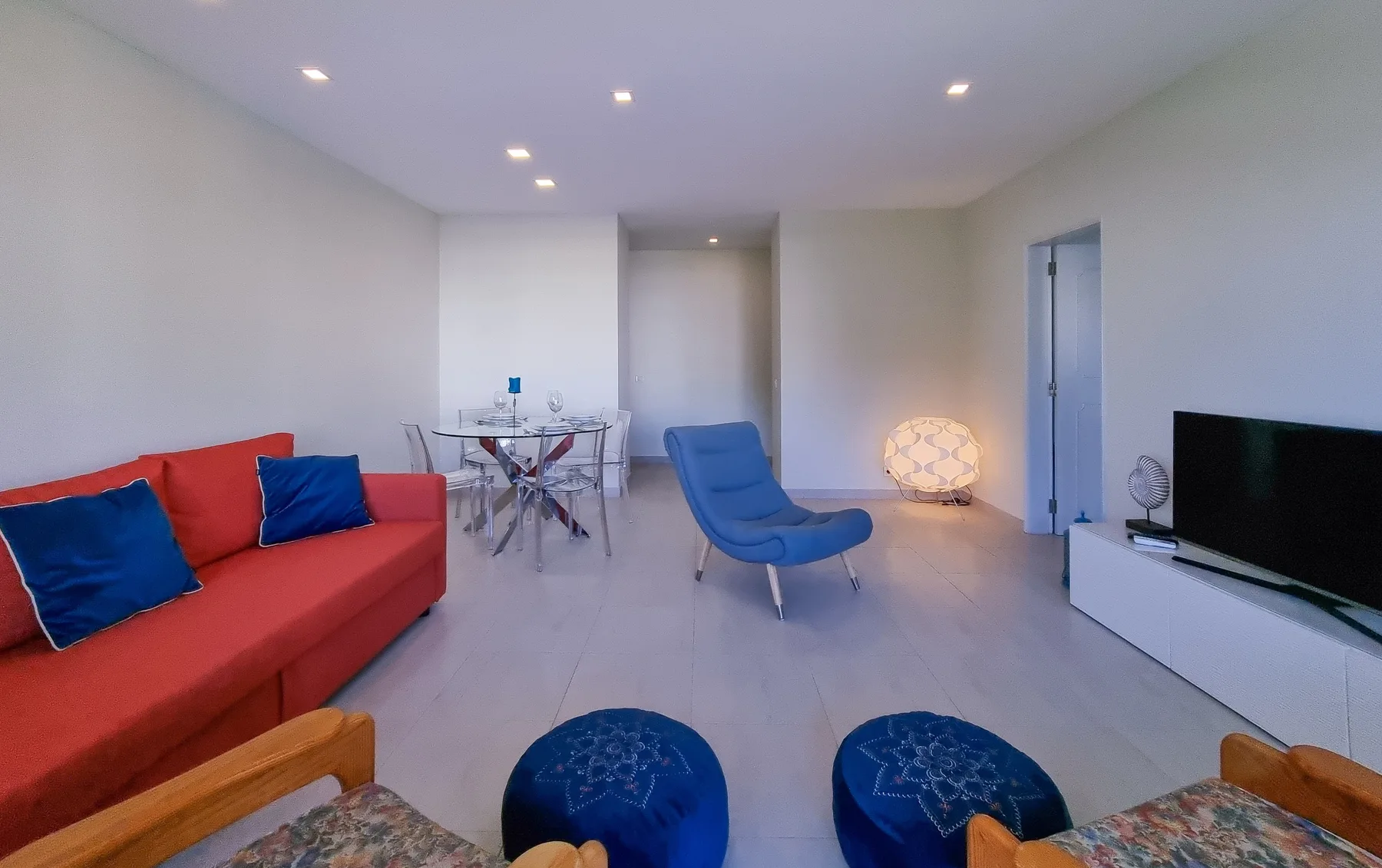 Una sala luminosa con un sofá rojo, asientos azules y un televisor.