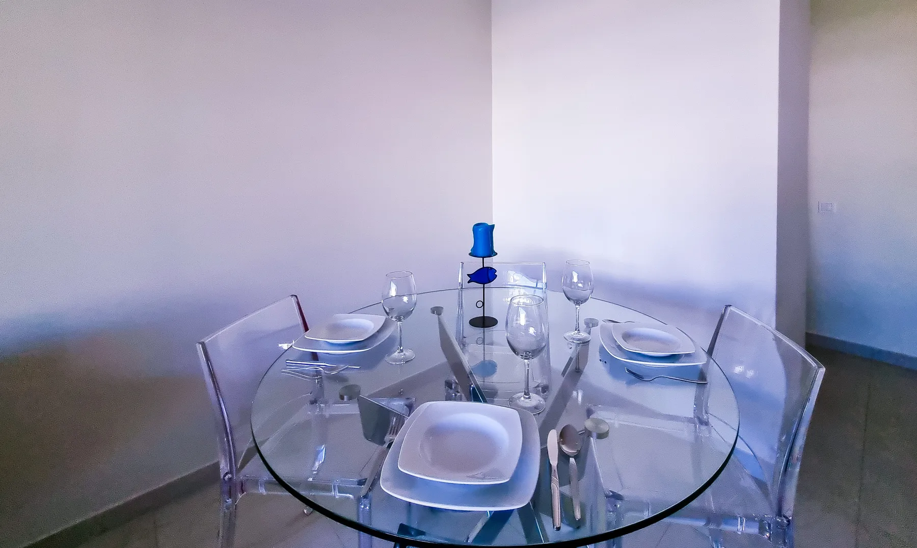 Comedor con una mesa de cristal preparada con platos y copas.