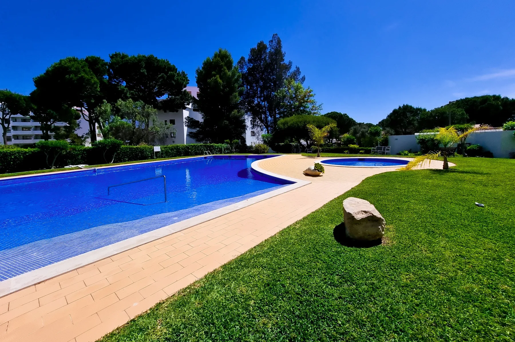 Una piscina al aire libre bordea un camino pavimentado y un césped.