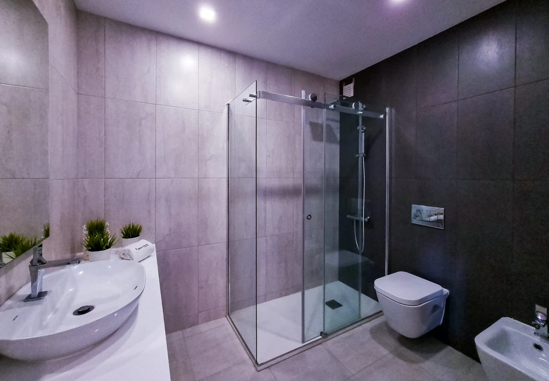 Un baño moderno con ducha de cristal, lavabo e inodoro.