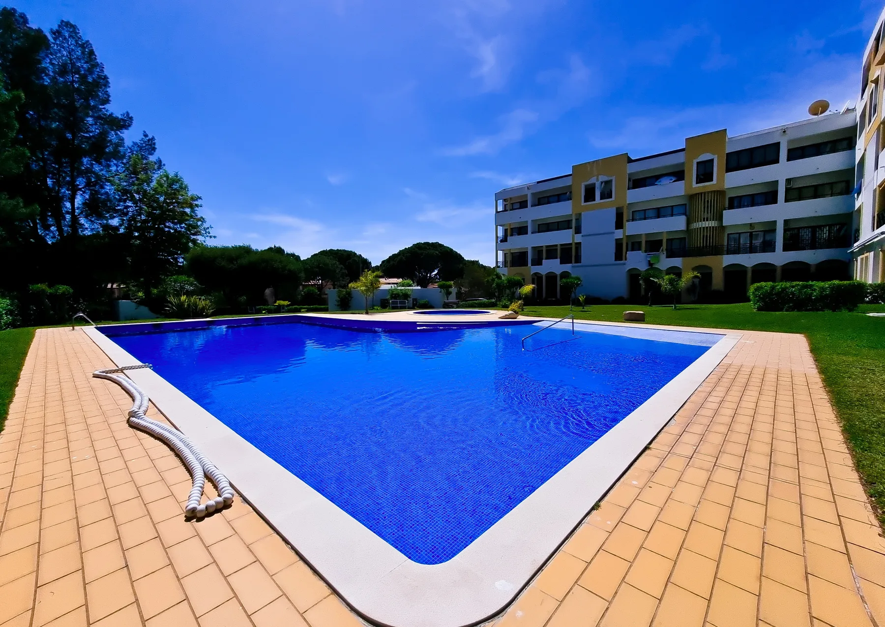 Una piscina al aire libre está junto a una terraza pavimentada y un edificio de apartamentos.