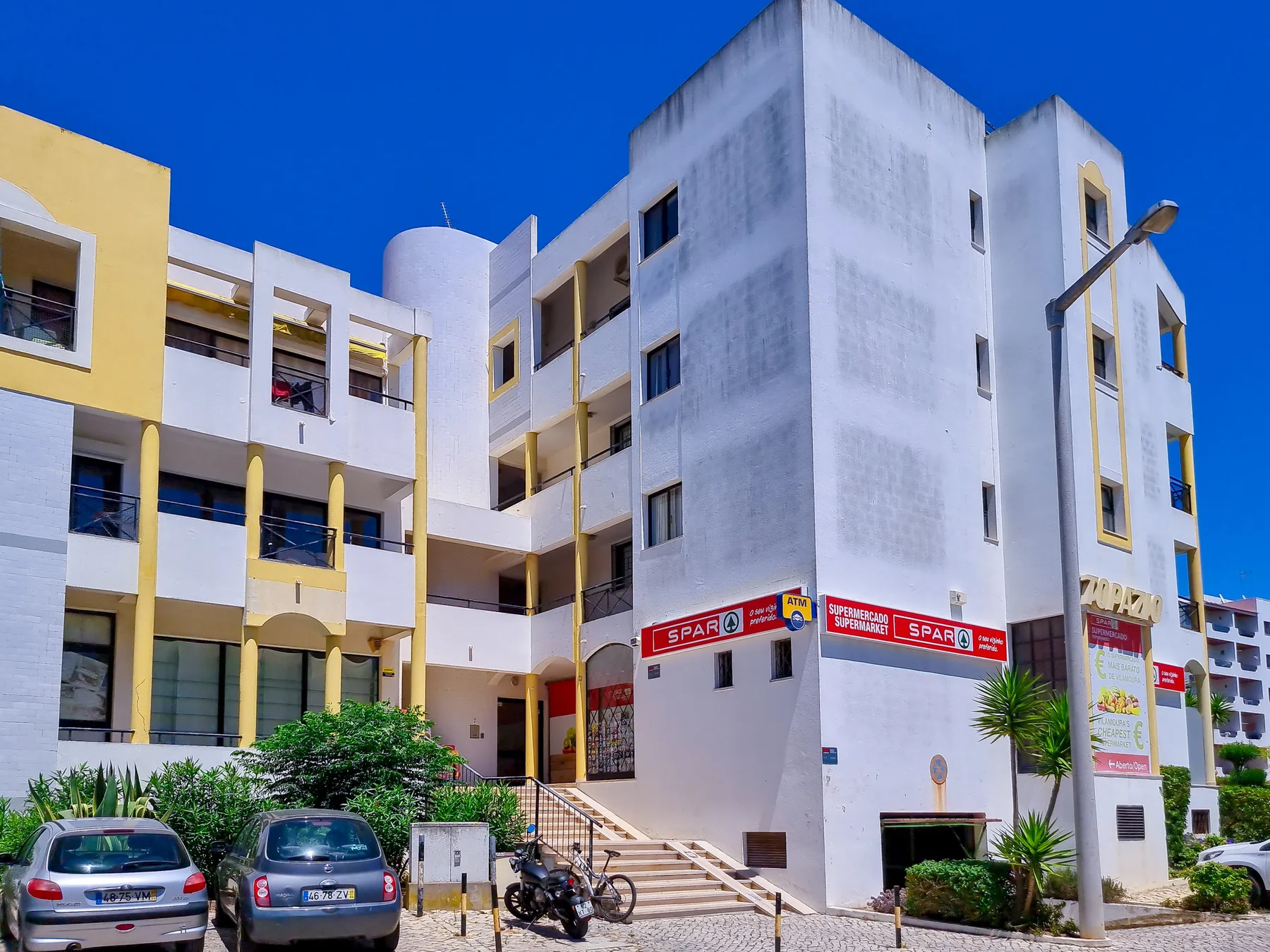 Un edificio de apartamentos blanco con detalles amarillos está junto a una calle.