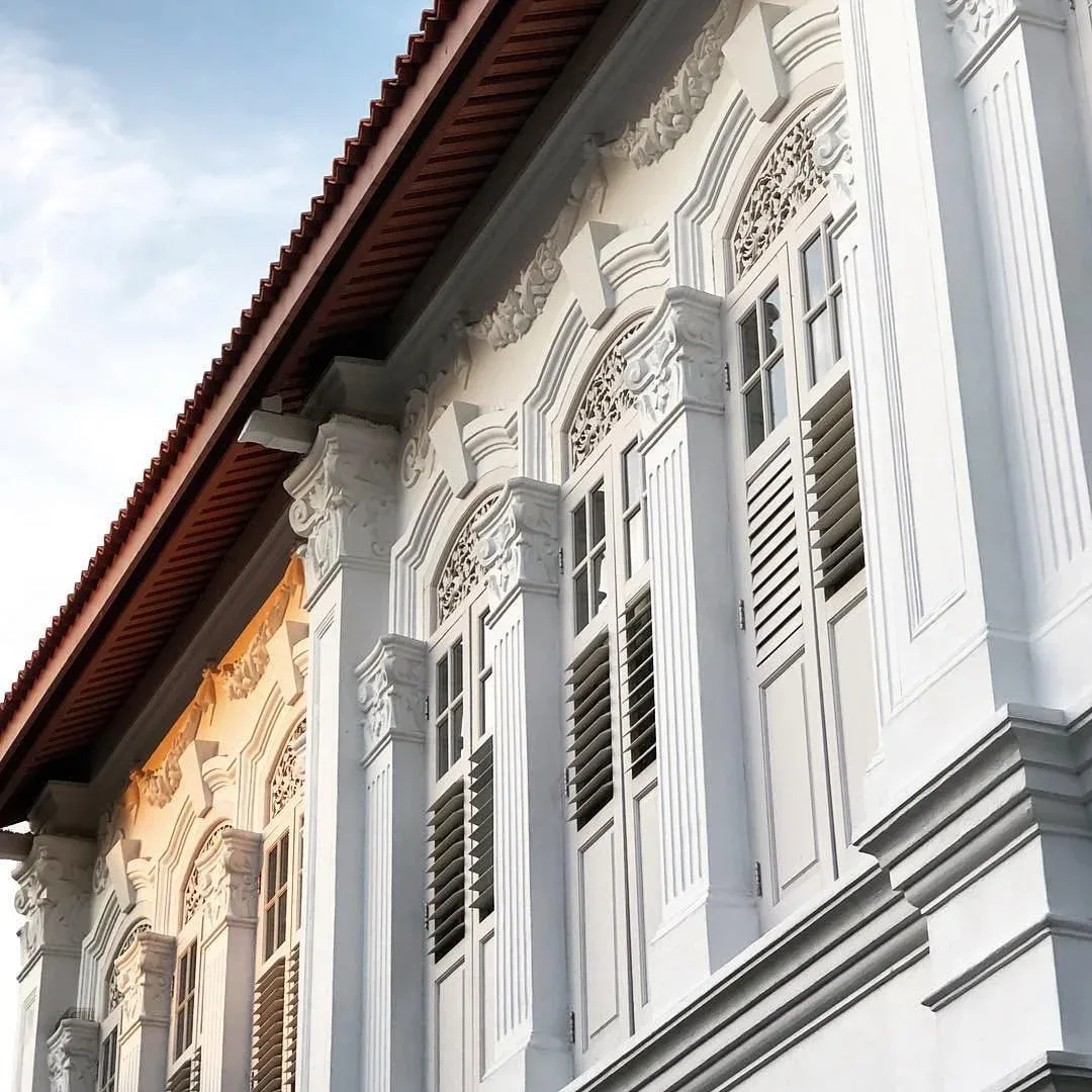 Fachada blanca de un edificio histórico con contraventanas decorativas y tejado de tejas rojas.