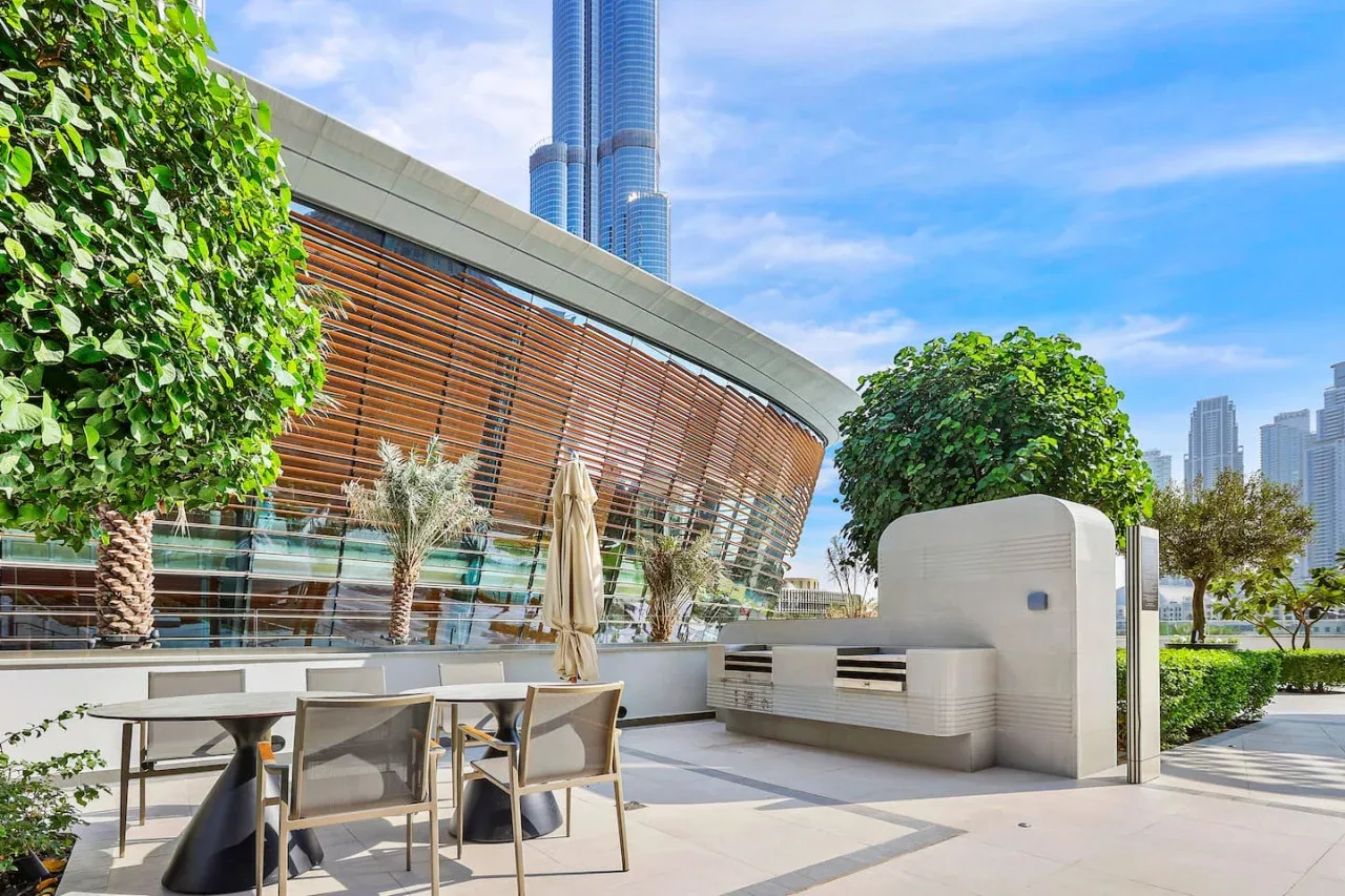Una terraza al aire libre con asientos para comer junto a un edificio curvo y vegetación.