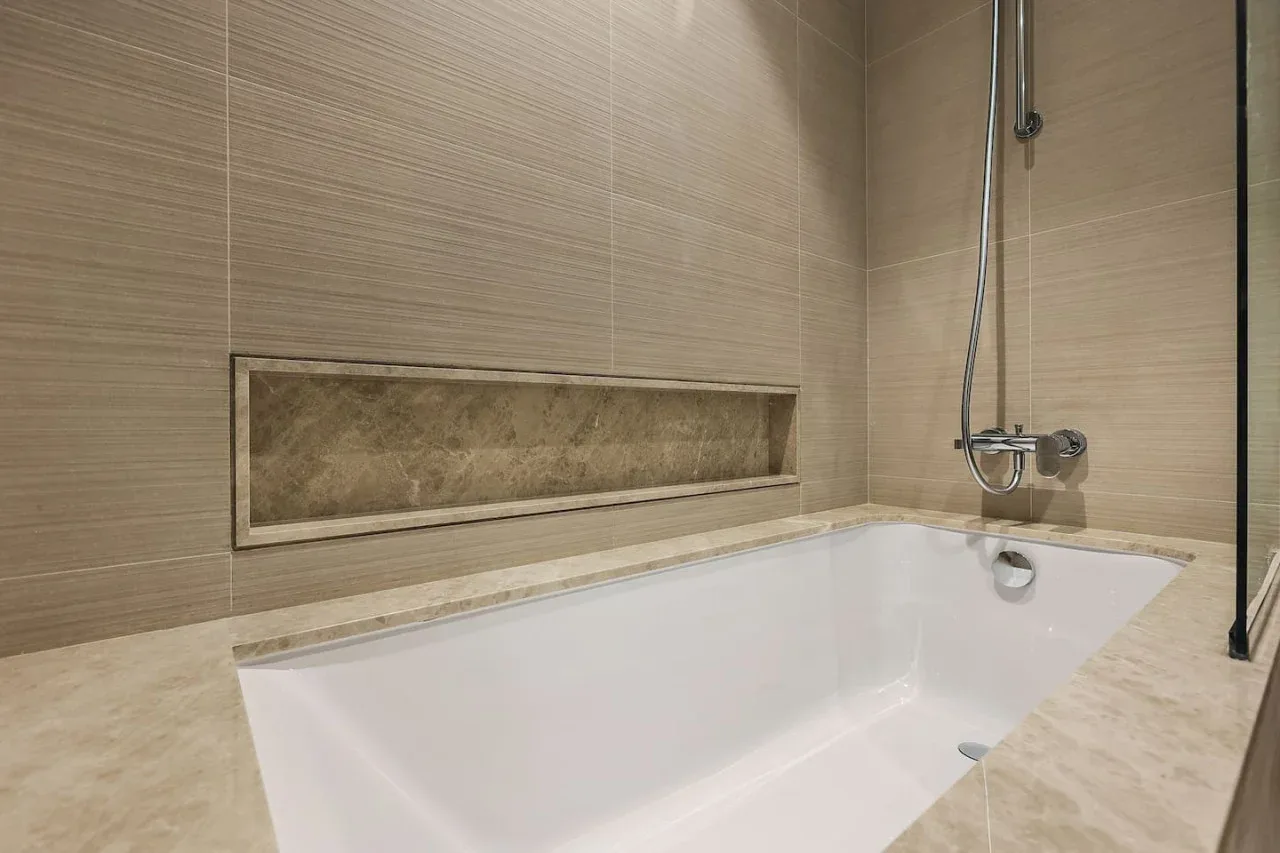 Una bañera y una ducha están junto a paredes de azulejos beige.