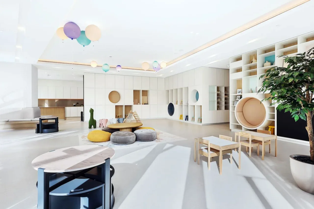 Una luminosa sala de juegos infantil con mesas bajas, sillas pequeñas y cojines de colores.