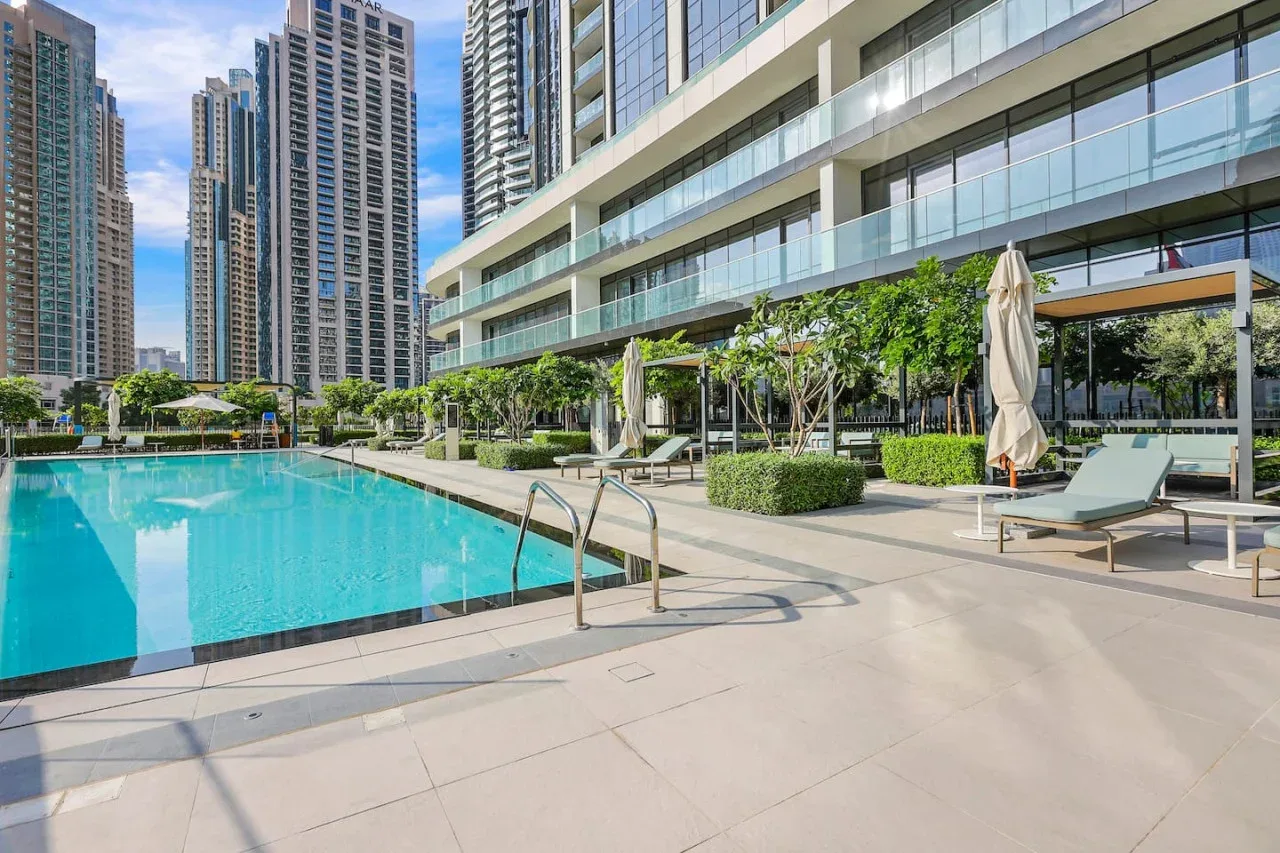 Una piscina al aire libre junto a un edificio moderno, con asientos en la terraza.