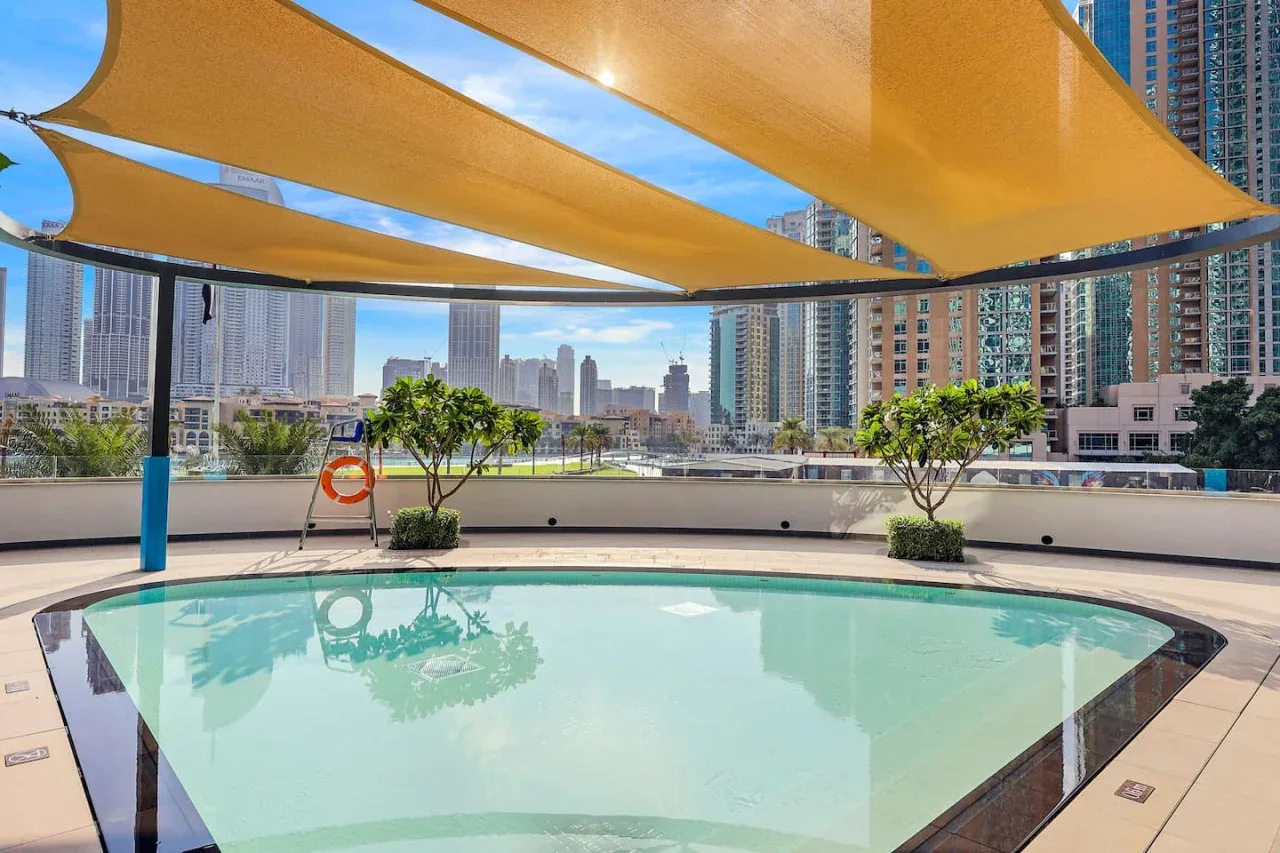 Una piscina en la azotea está bajo toldos de sombra, con edificios al fondo.