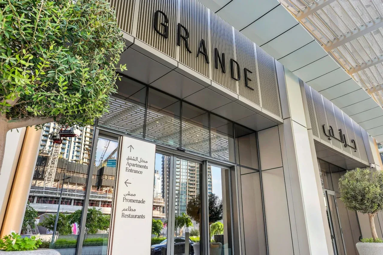 Entrada de un edificio moderno con puertas de vidrio y un letrero destacado que dice GRANDE.