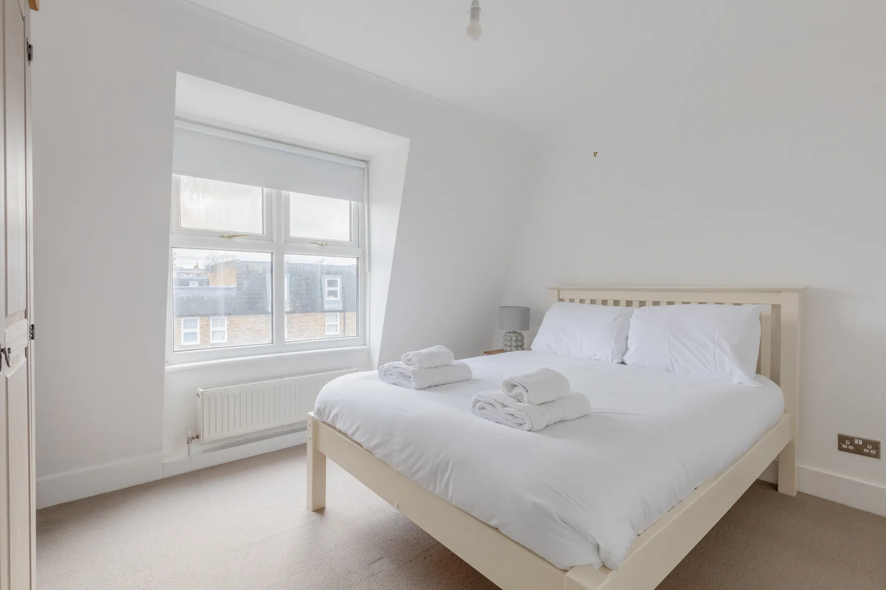 A bright bedroom with a large bed and a window overlooking nearby buildings.