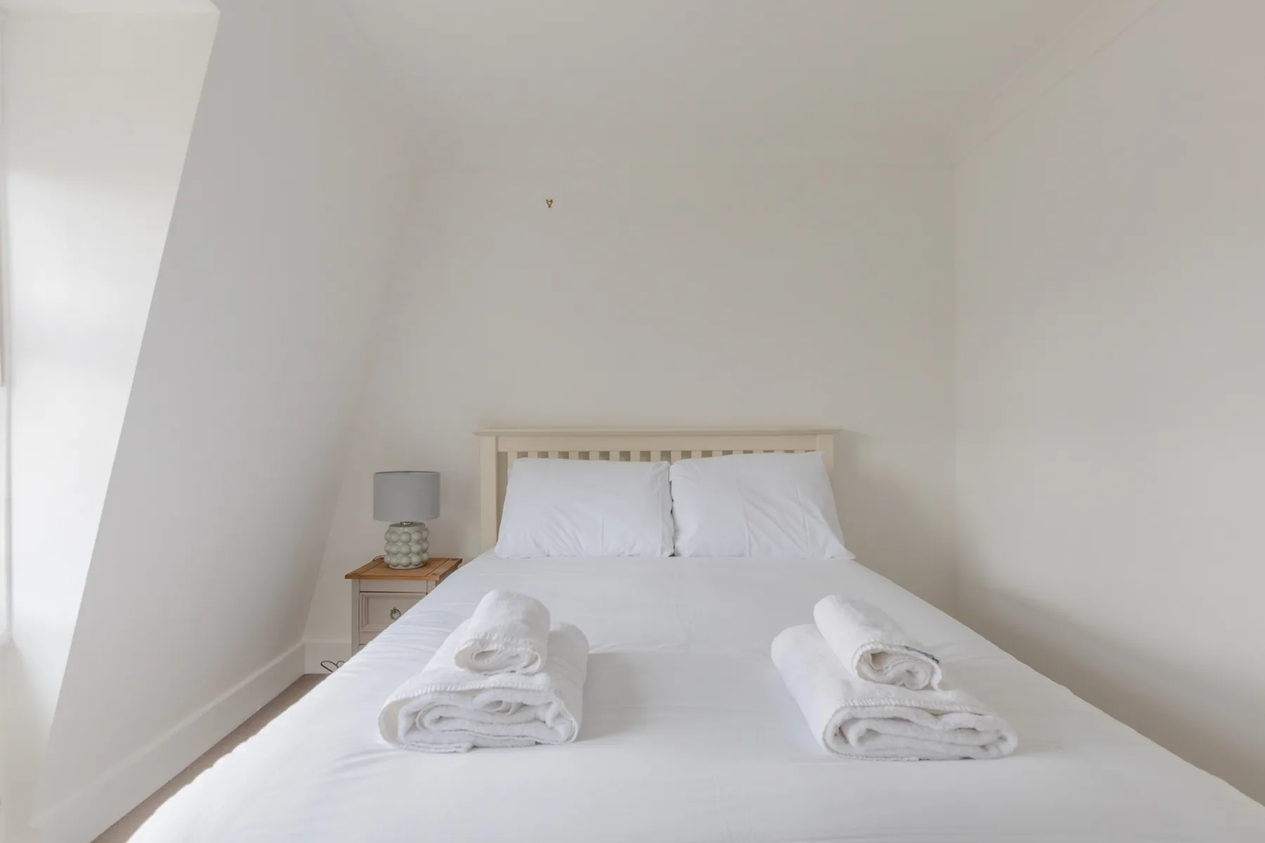 A bedroom with a neatly made bed and folded towels.