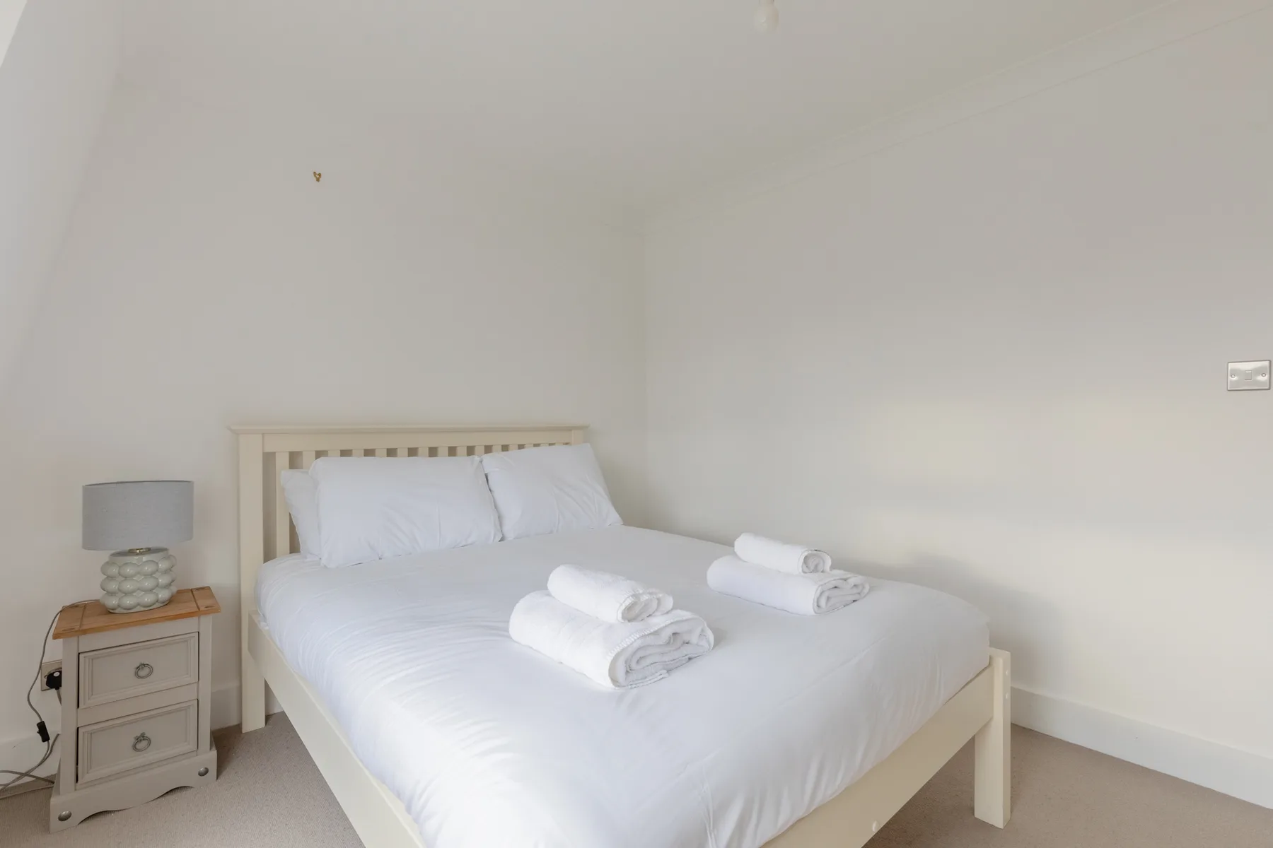 A bright bedroom with a neatly made bed and a bedside table.