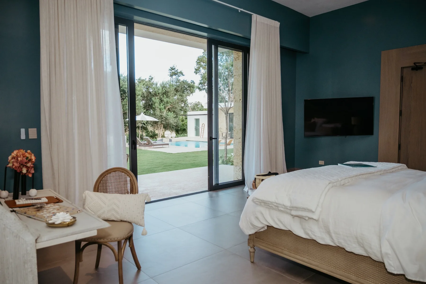 Un dormitorio con una cama junto a puertas de vidrio que dan a una zona ajardinada con piscina.