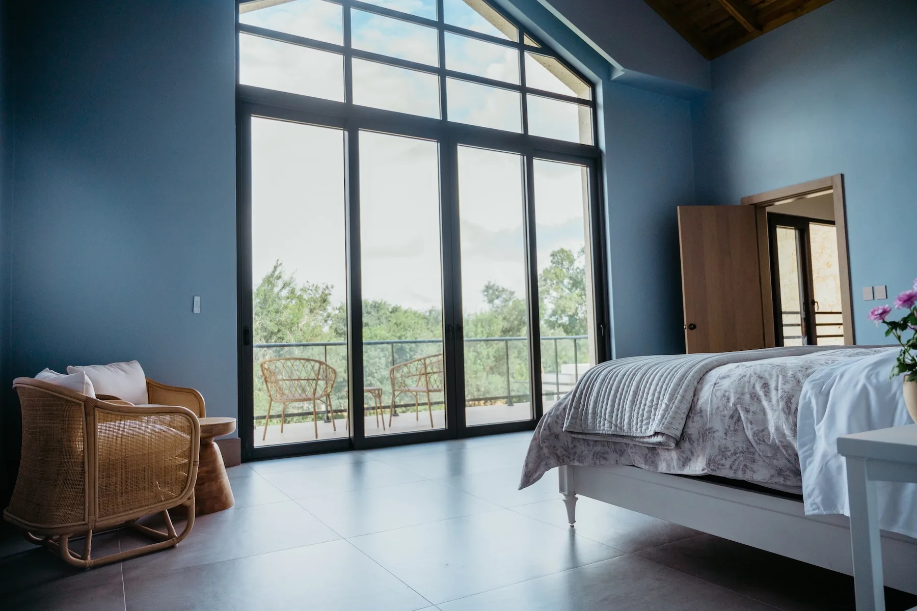 Un dormitorio con una cama junto a ventanas altas y una pequeña zona de asientos.