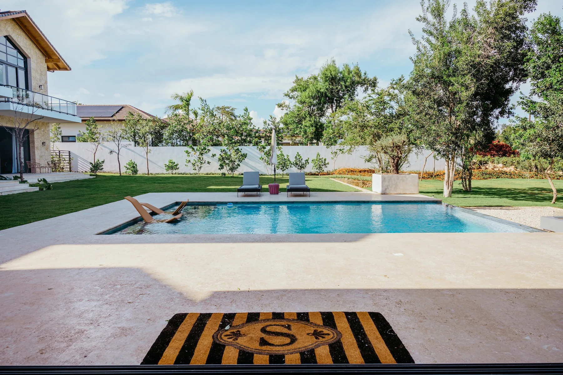 Una piscina exterior está junto a un césped y un jardín ajardinado.