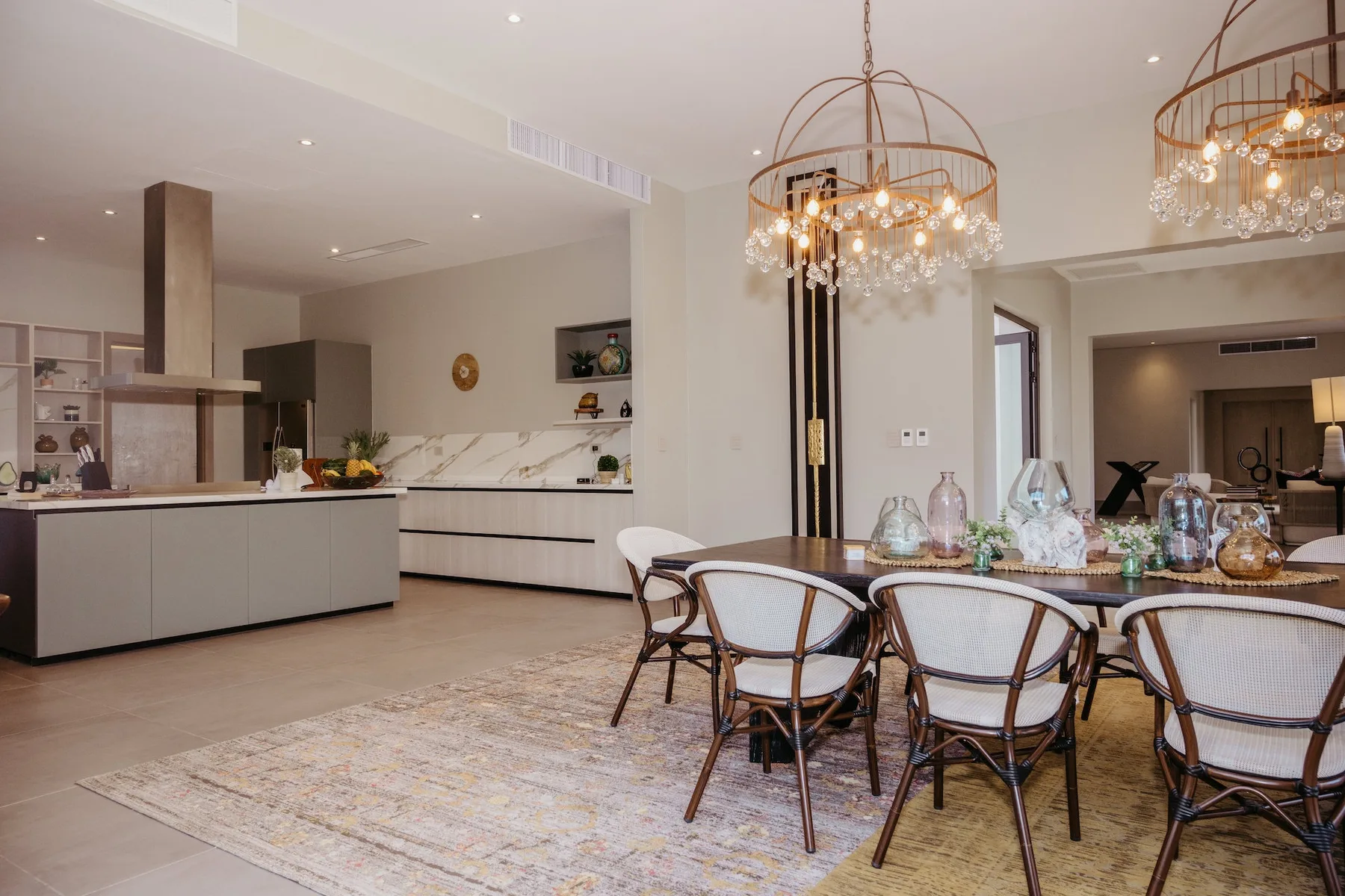 Comedor con una mesa larga, sillas y lámparas colgantes junto a una cocina abierta.