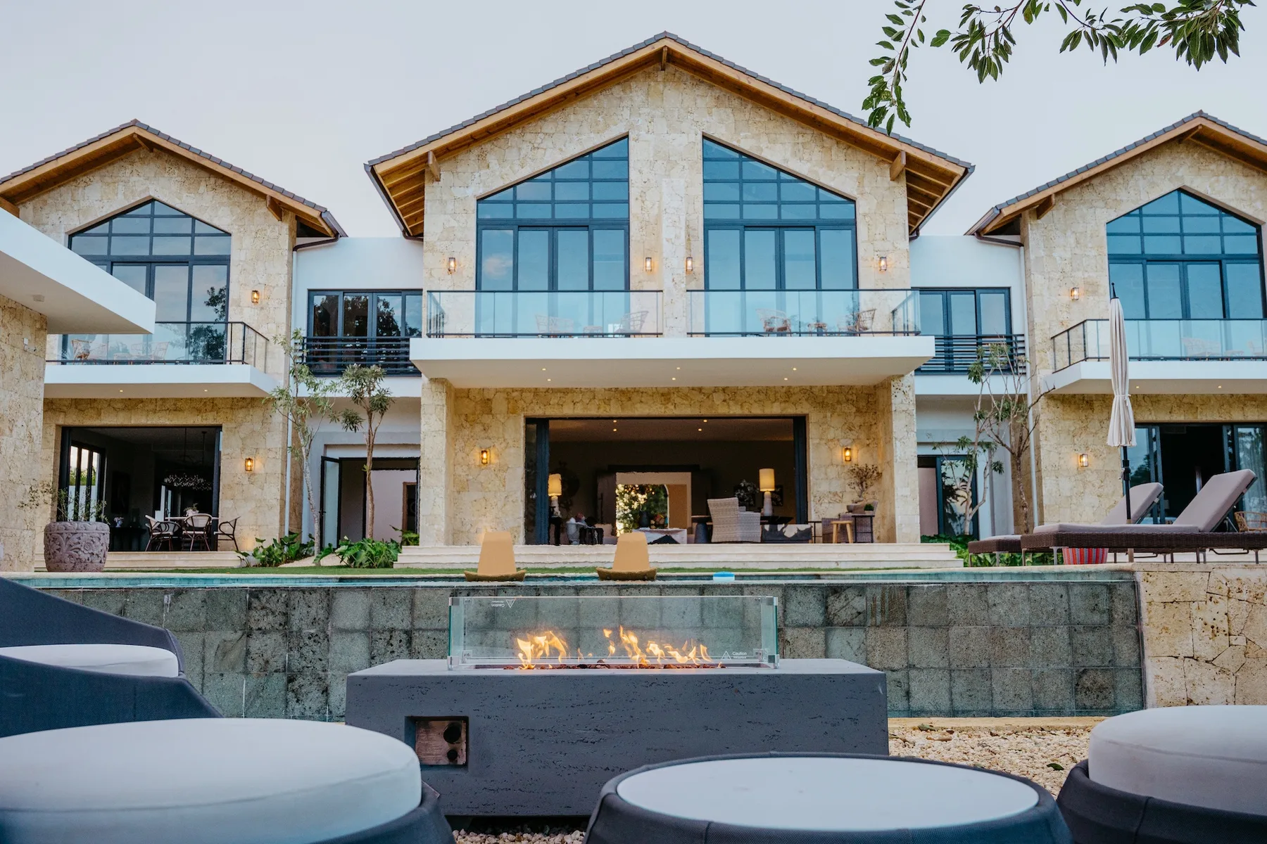 Una casa moderna de varios tejados a dos aguas da a una piscina, con una chimenea exterior al frente.